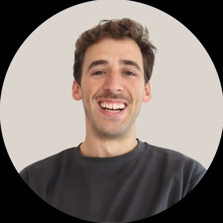 Smiling young man with short, curly hair, wearing a dark top, against a light background in a circular frame.