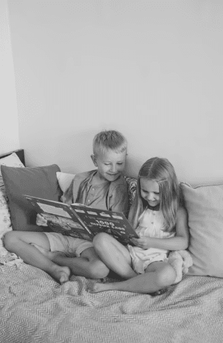 A circle of people sitting cross-legged, meditating with hands in a prayer position. Soft, warm lighting.