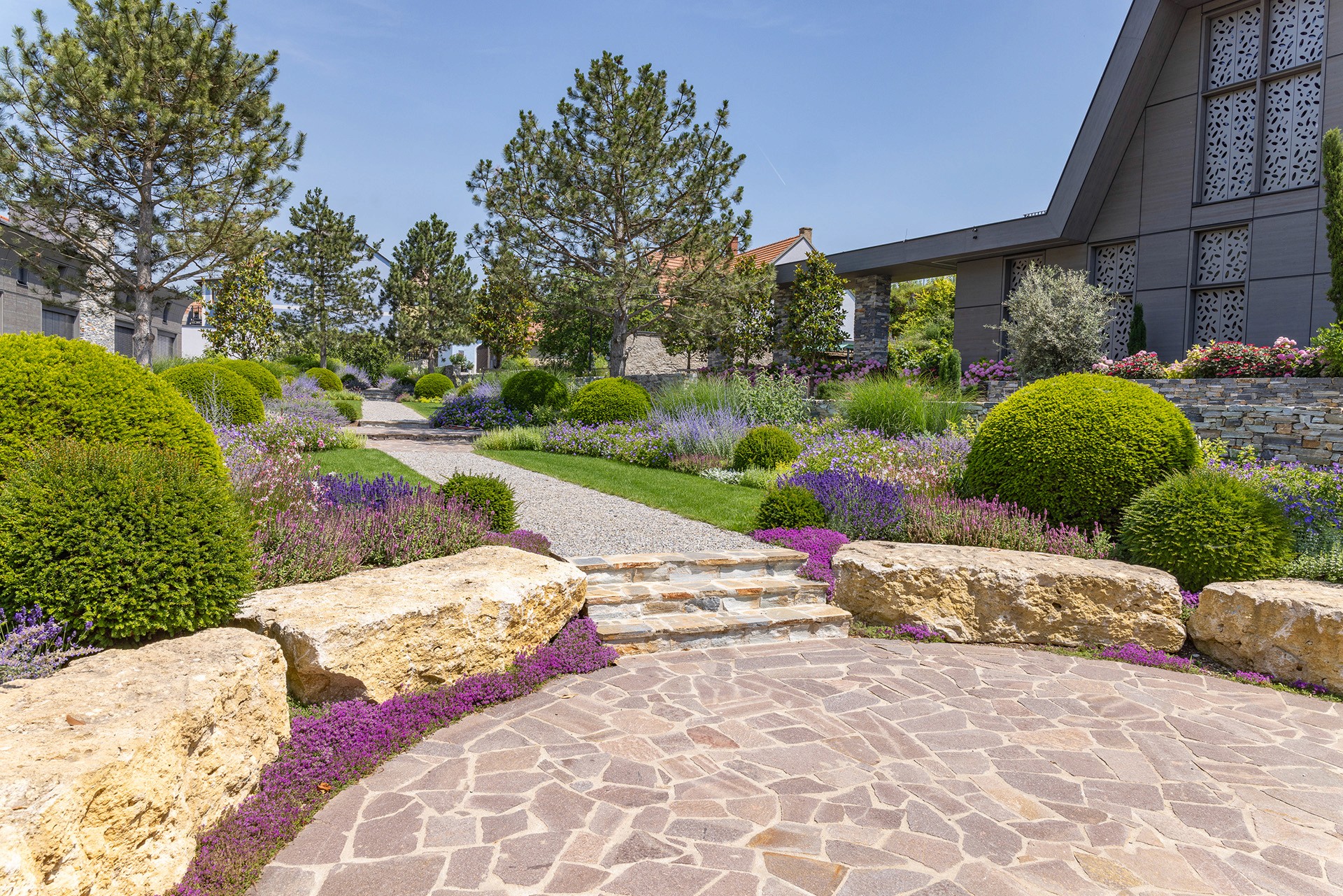 Gestalteter Garten mit Natursteinflächen, Staudenbeeten und formgeschnittenen Sträuchern.