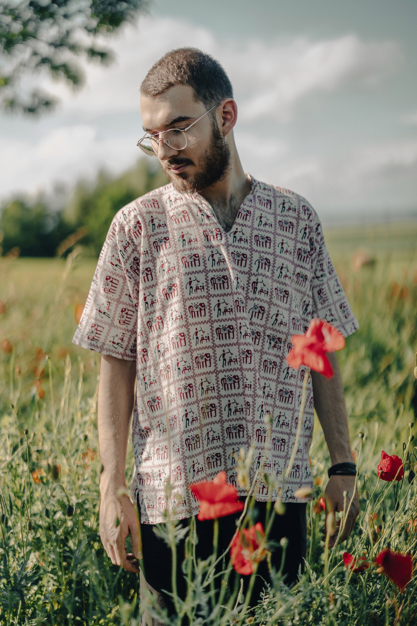 Szakállas férfi áll világos ingben, pipacsokkal teli mezőn, napsütéses, nyári hangulatban.