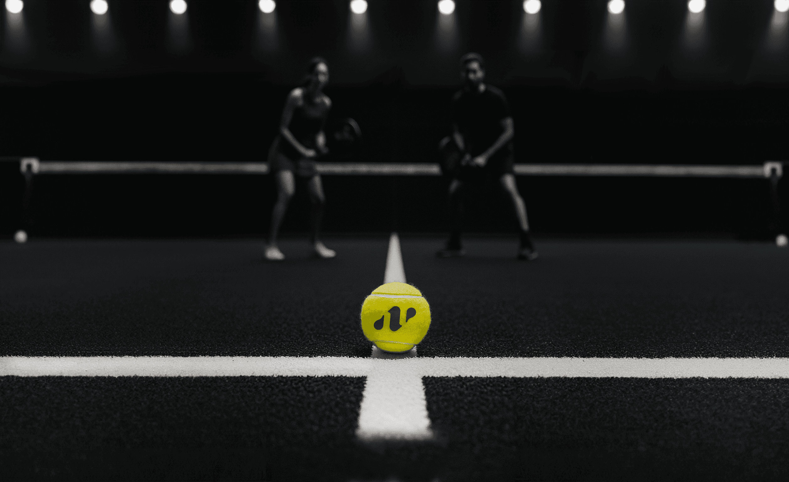 Gelber Padelball mit Padelnero-Logo liegt im Fokus auf schwarzem Court, im Hintergrund stehen zwei Spieler bereit zum Match – Spannung und Design vereint in einem Bild.