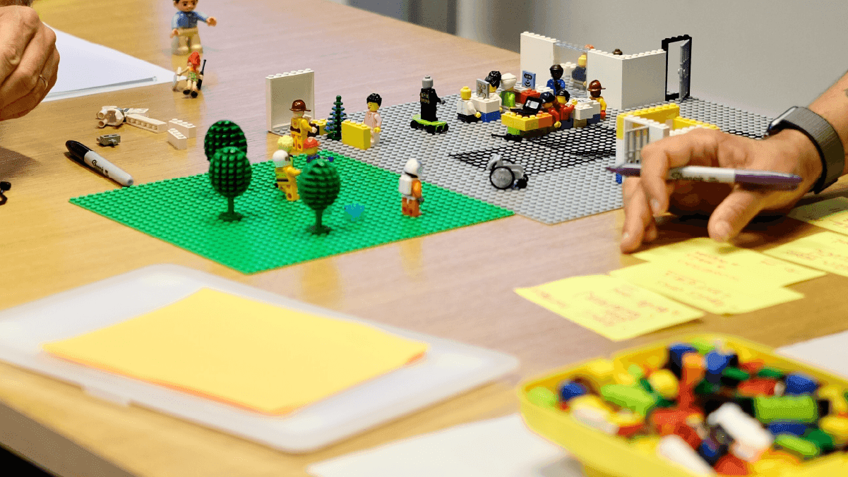 Lego prototype of a user journey scene with minifigures, trees, and buildings on baseplates during a workshop