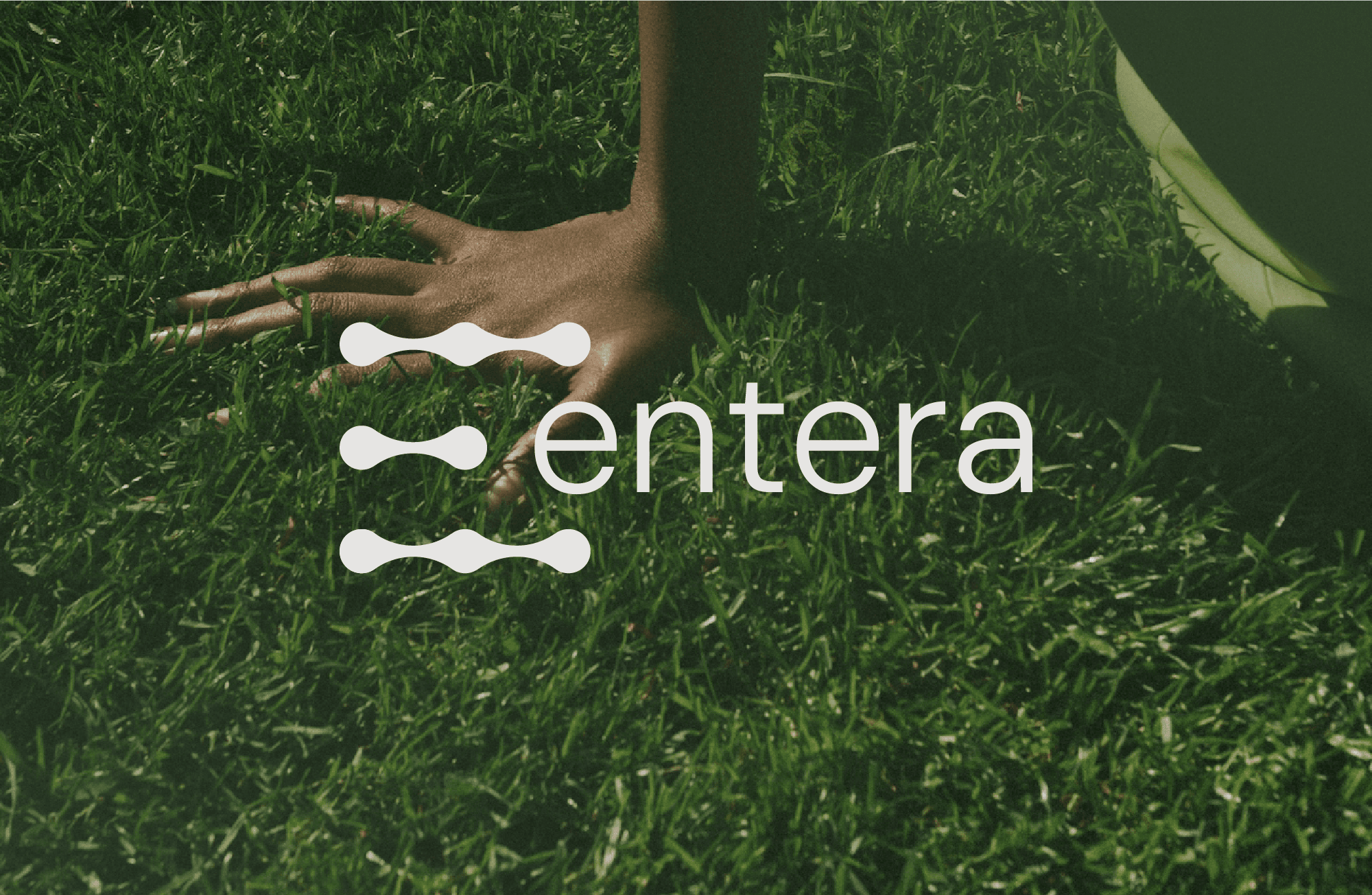 Entera logo over a photo of a hand touching grass
