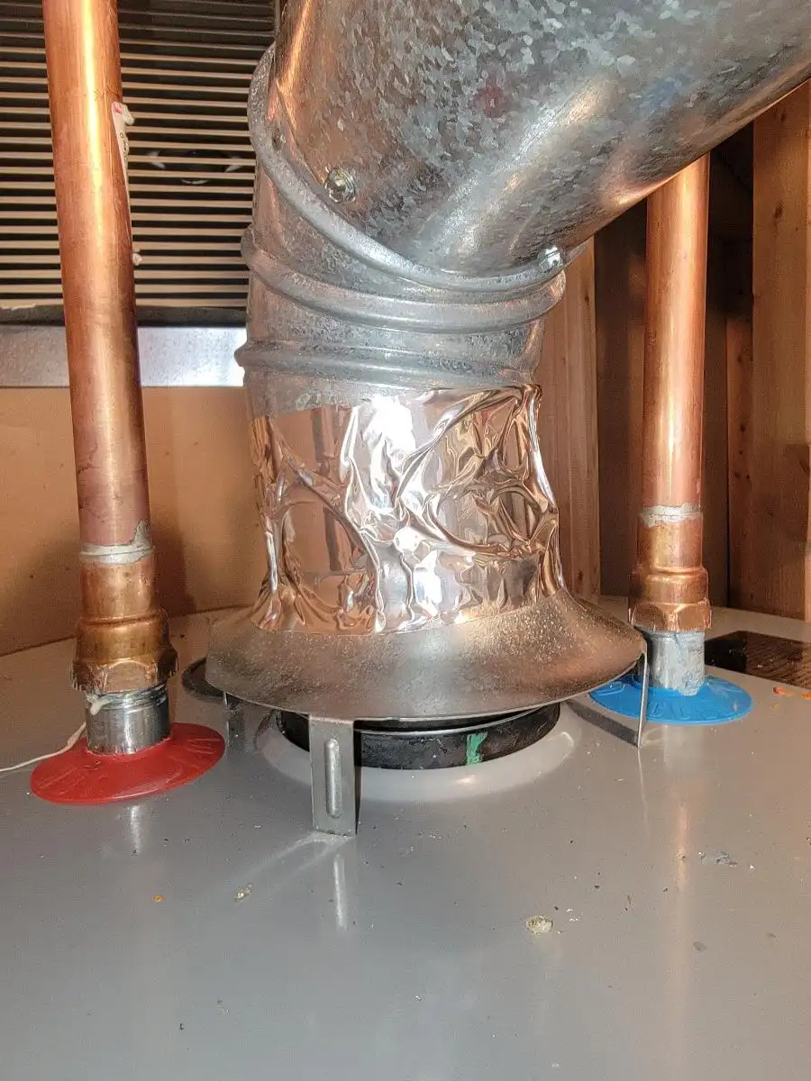 A close-up view of a gas water heater's draft hood, exhaust vent, and copper piping connections during a professional water heater repair and inspection.
