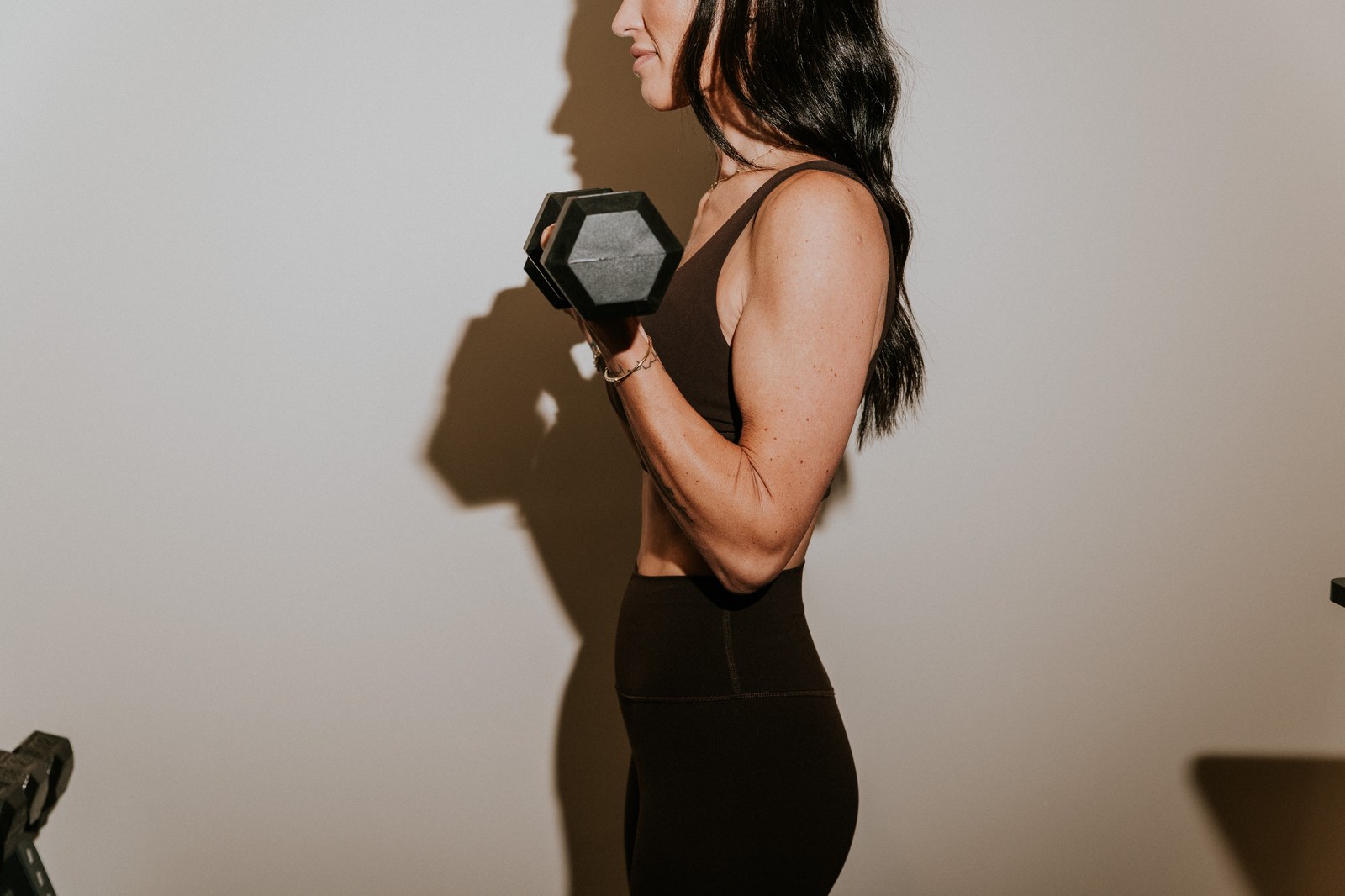 A woman lifting a dumbbell in warm side light, working to protect lean mass.