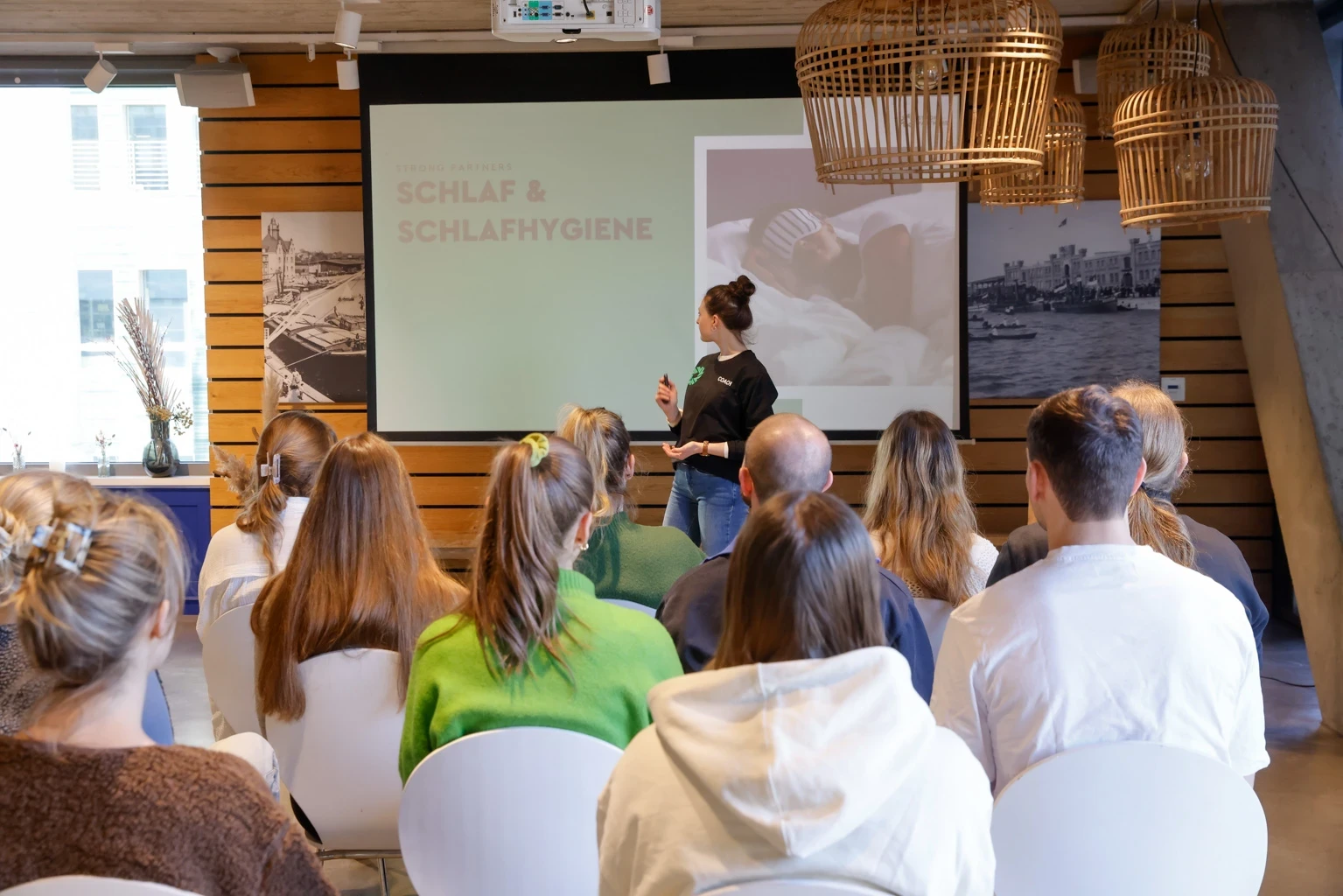 Junge Frau steht vor Publikum auf der Bühne, im Hintergrund eine Präsentation