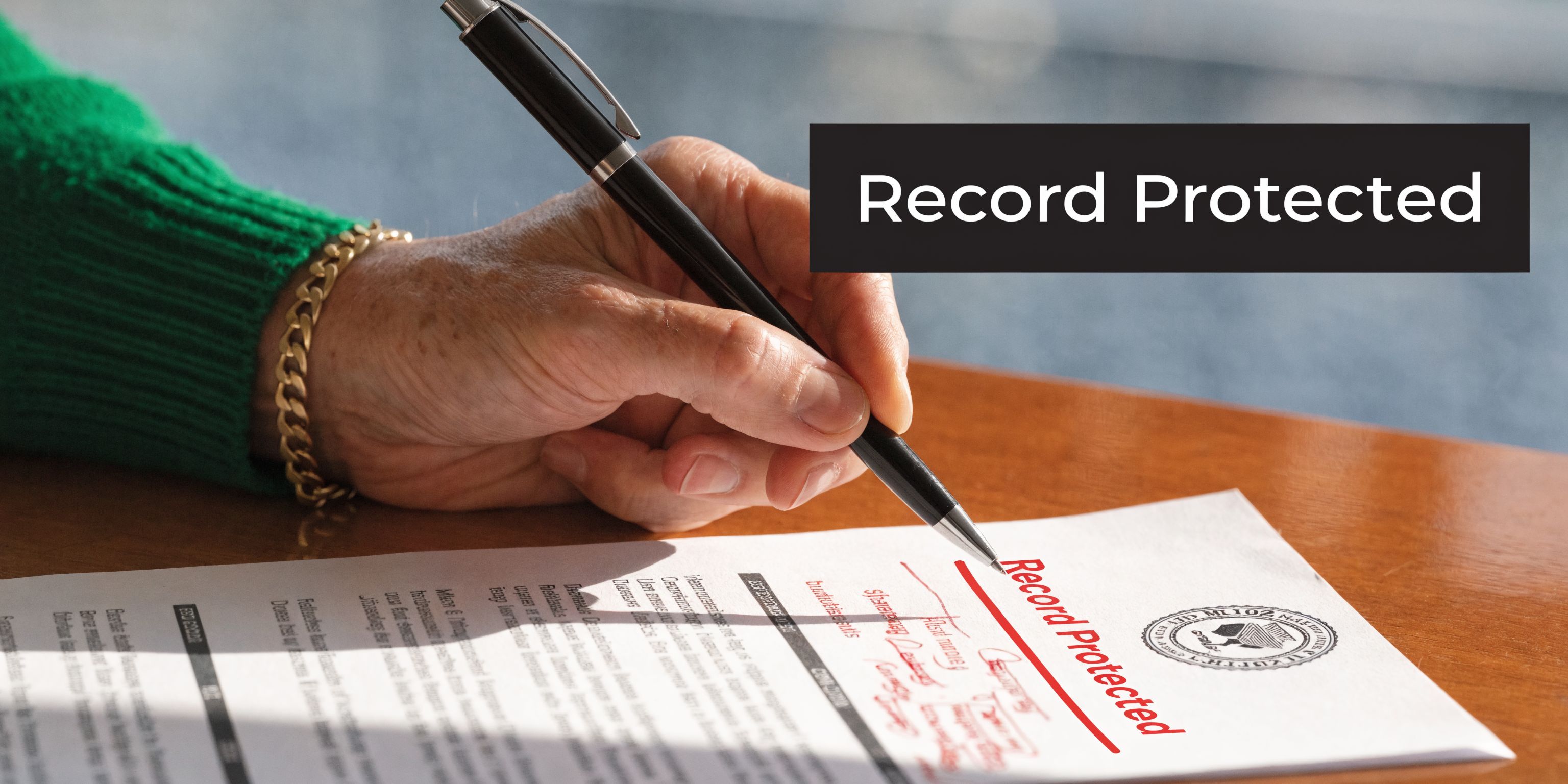 A close-up view of an elderly person's hand signing a document labeled as record protected.