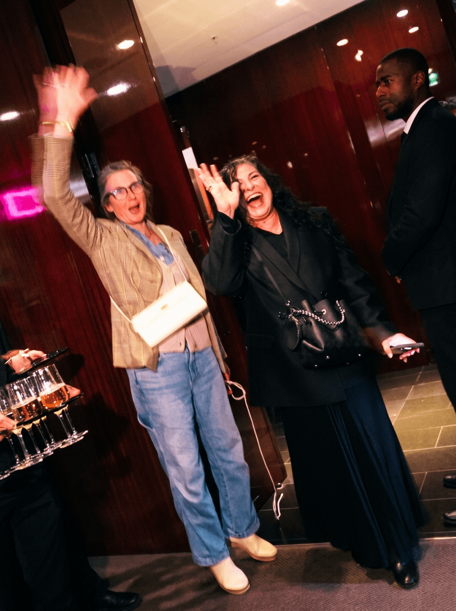 Bride sitting on ground against wall, groom standing nearby