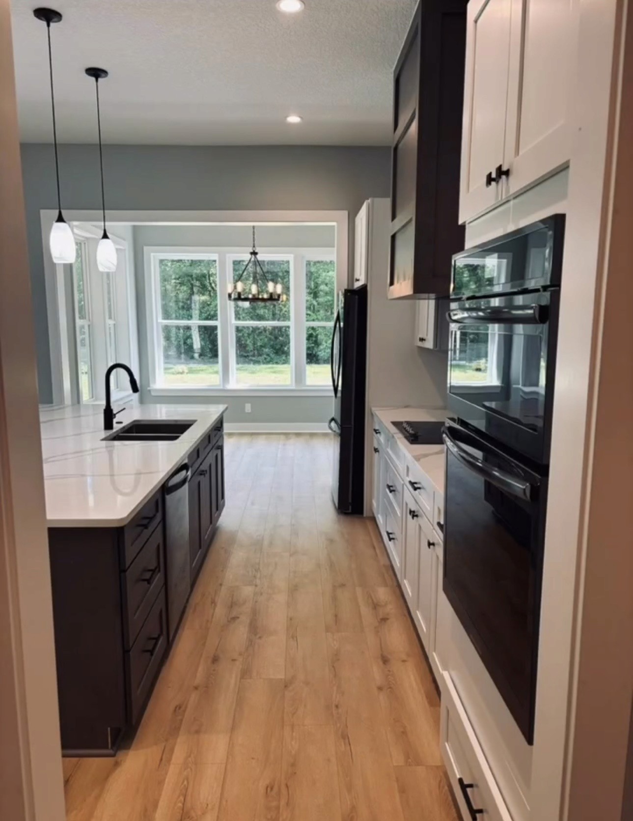 Galley view of kitchen with dark island, black appliances, chandelier, and green view through windows