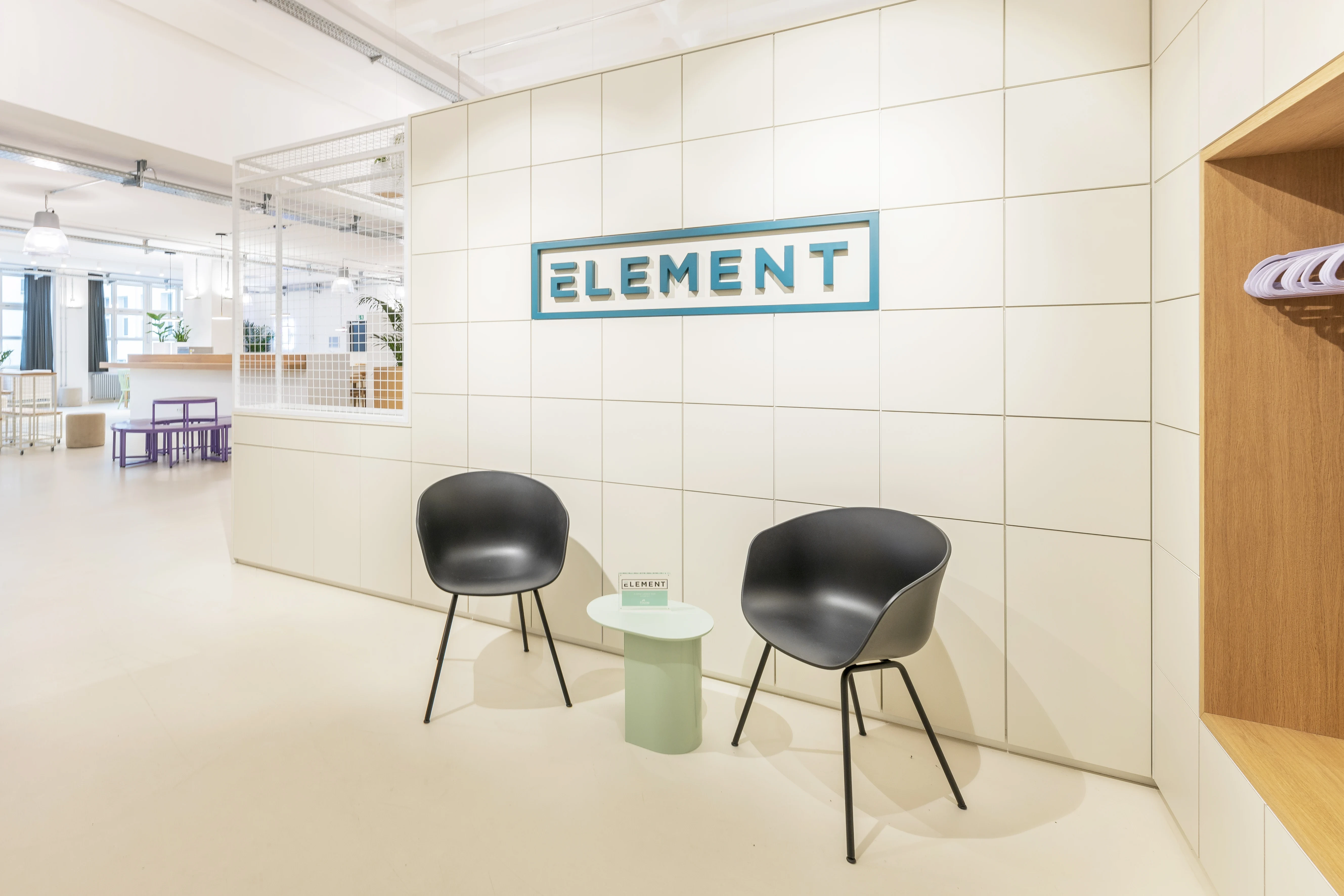 Waiting corner at ELEMENT with two black shell armchairs around a mint-green side table, in front of a white tiled wall with the turquoise-framed ELEMENT logo.