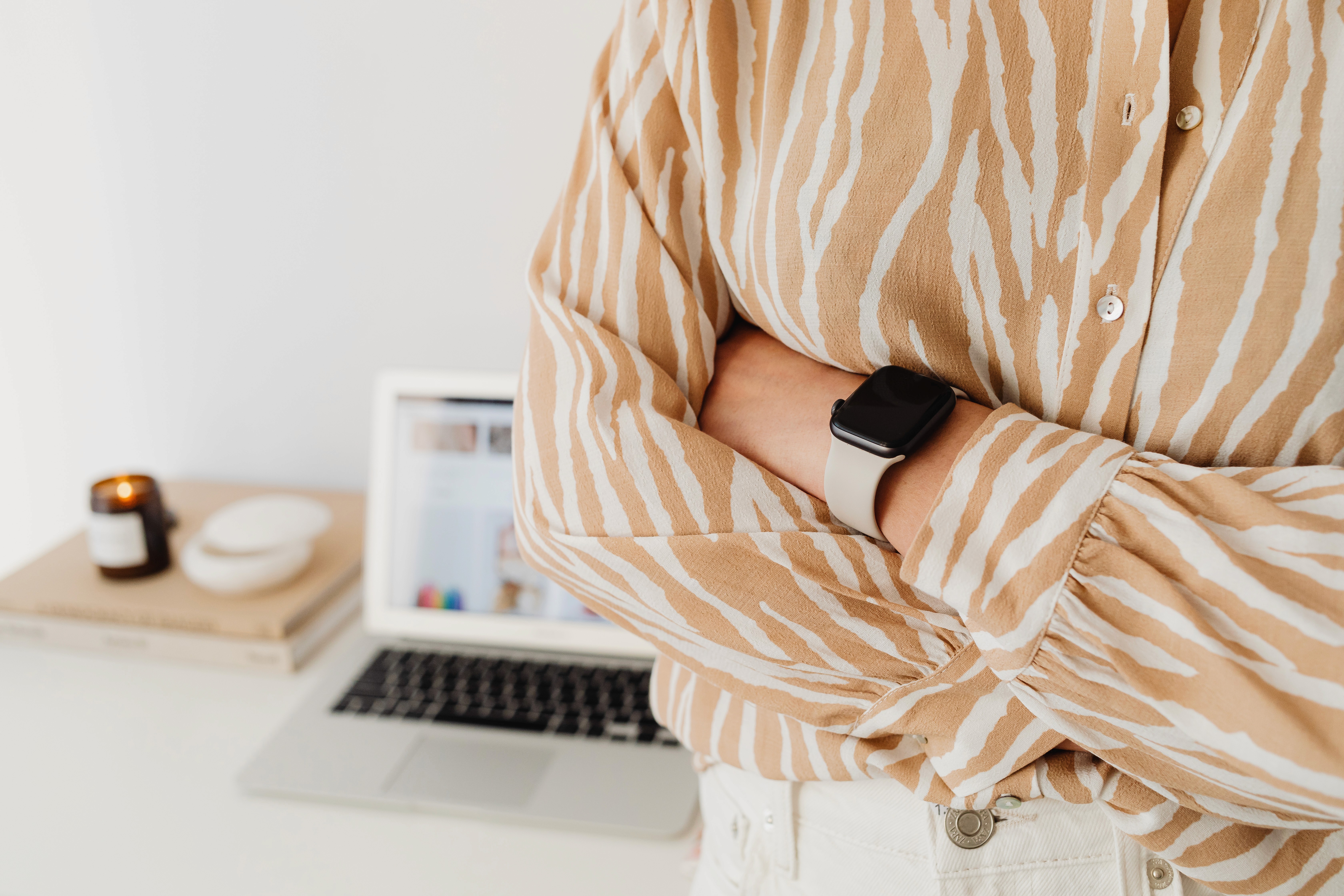 Person wearing a striped shirt with arms crossed, standing beside an open laptop on a desk.