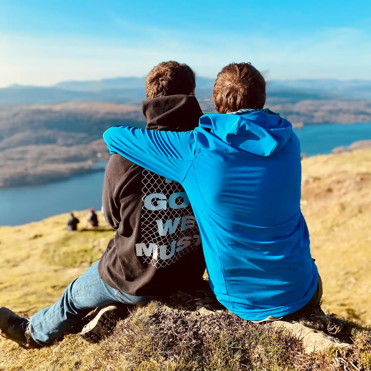 Two men sitting together outdoors, embracing while overlooking a scenic view, symbolizing connection and healing through gay-affirming therapy in Los Angeles.