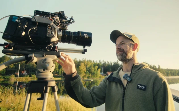 A cinematographer adjusting a cinema camera with a DZOFILM Arles zoom lens outdoors at sunset