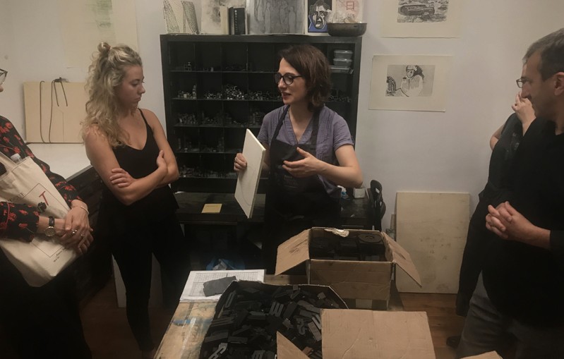 A photo of two girls talking to each other while standing in a printing workshop.