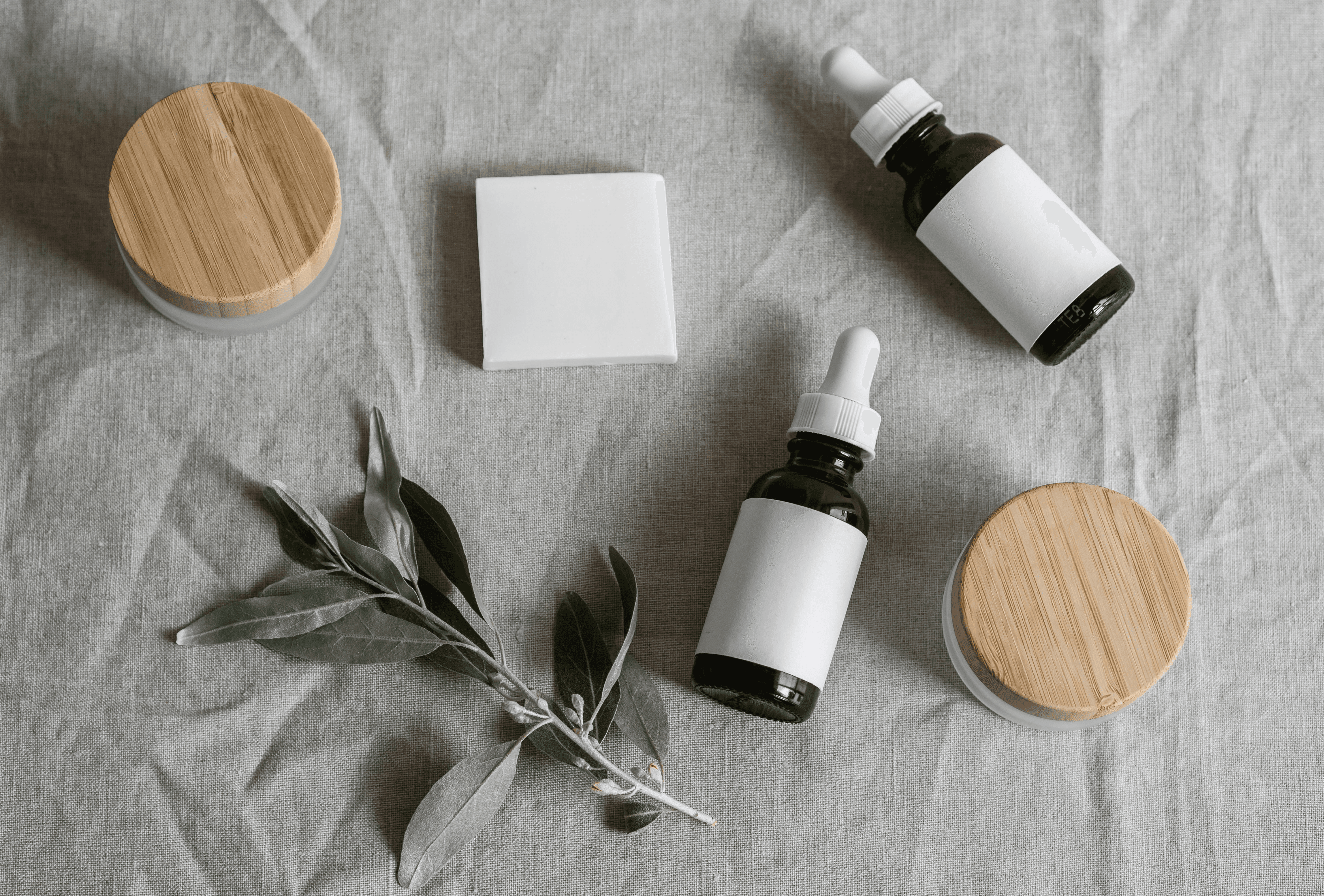 Spa products: skincare serum bottles, cream jars, and soap bar on white cloth. Natural beauty products, self-care concept.