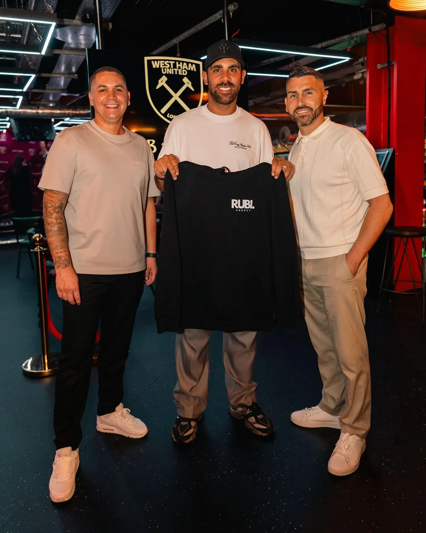 Three men pose while holding a black sweatshirt with white text.