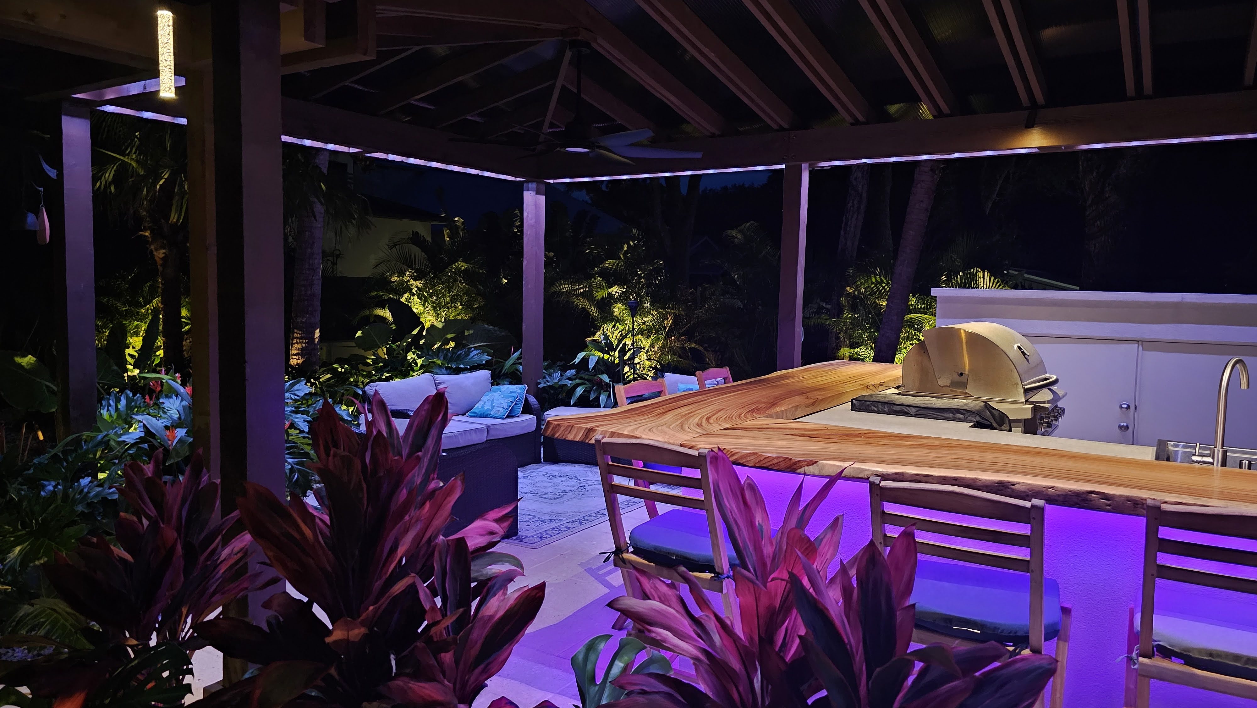 Pergola covered outdoor kitchen and lounge area with installed evening lighting