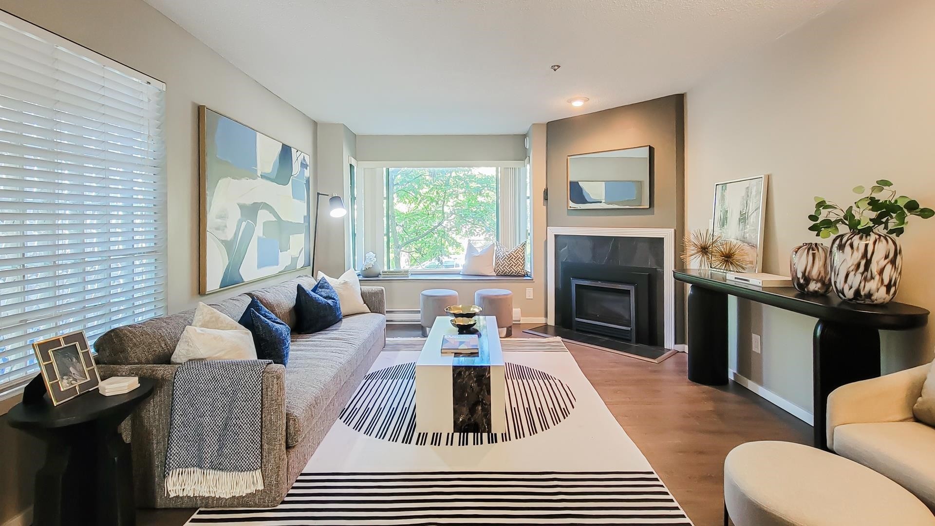 A modern living room featuring large windows, a cozy seating area, and a sleek fireplace against a light backdrop.