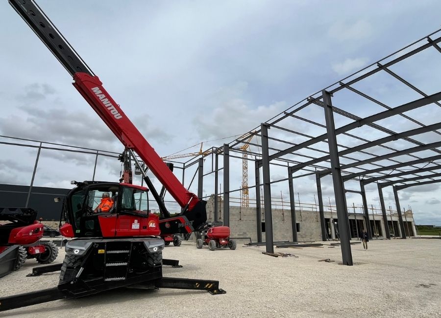 Chantier avec grue rouge en train de lever une poutre métallique pour montage de structure.