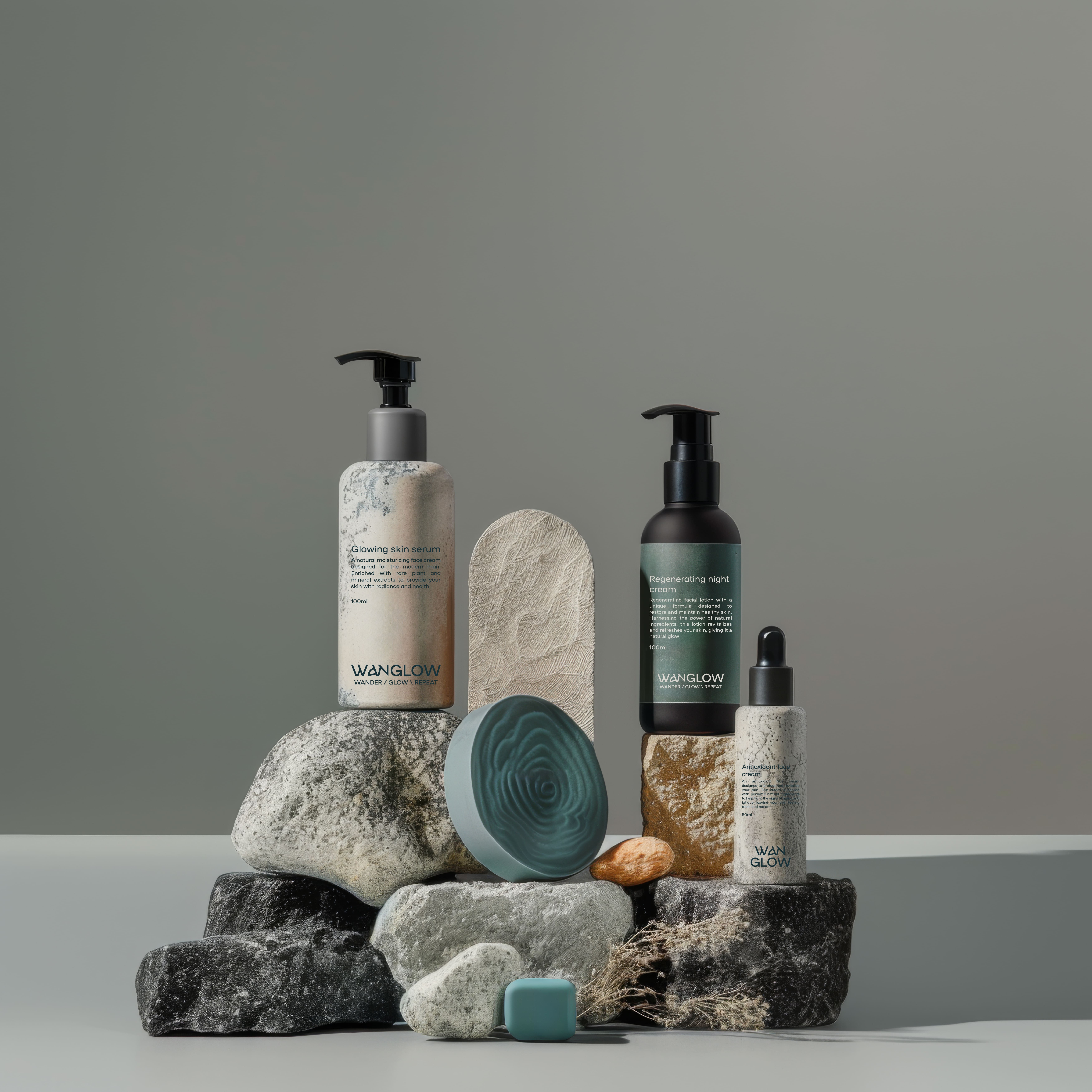A minimalist arrangement of skincare products on a stack of textured stones. The display features three bottles: a glowing skin serum in a matte gray container, a regenerating night cream in a sleek black pump bottle, and a smaller serum in a textured gray bottle. Beside them, there are smooth, turquoise-colored elements resembling soap, along with natural accents like a small almond and dried grass. The background is a soft gray, enhancing the serene aesthetic.