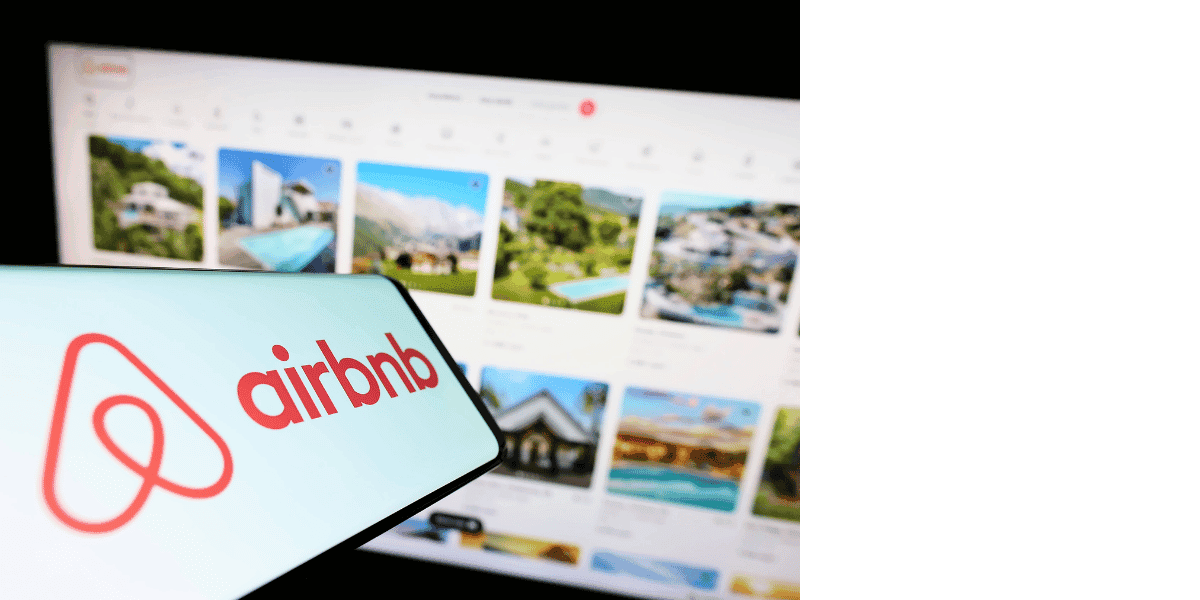Airbnb logo on a smartphone beside property listings