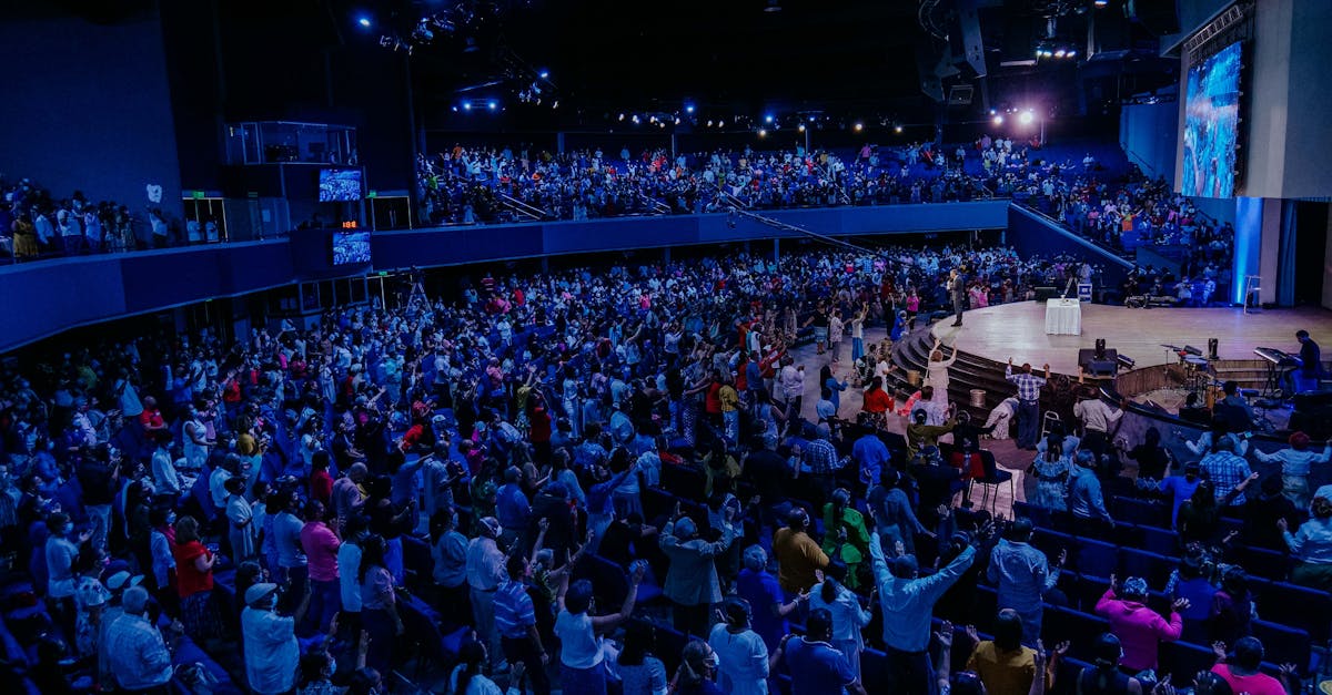 A large vibrant crowd enjoying a live performance in an indoor auditorium under blue lighting.