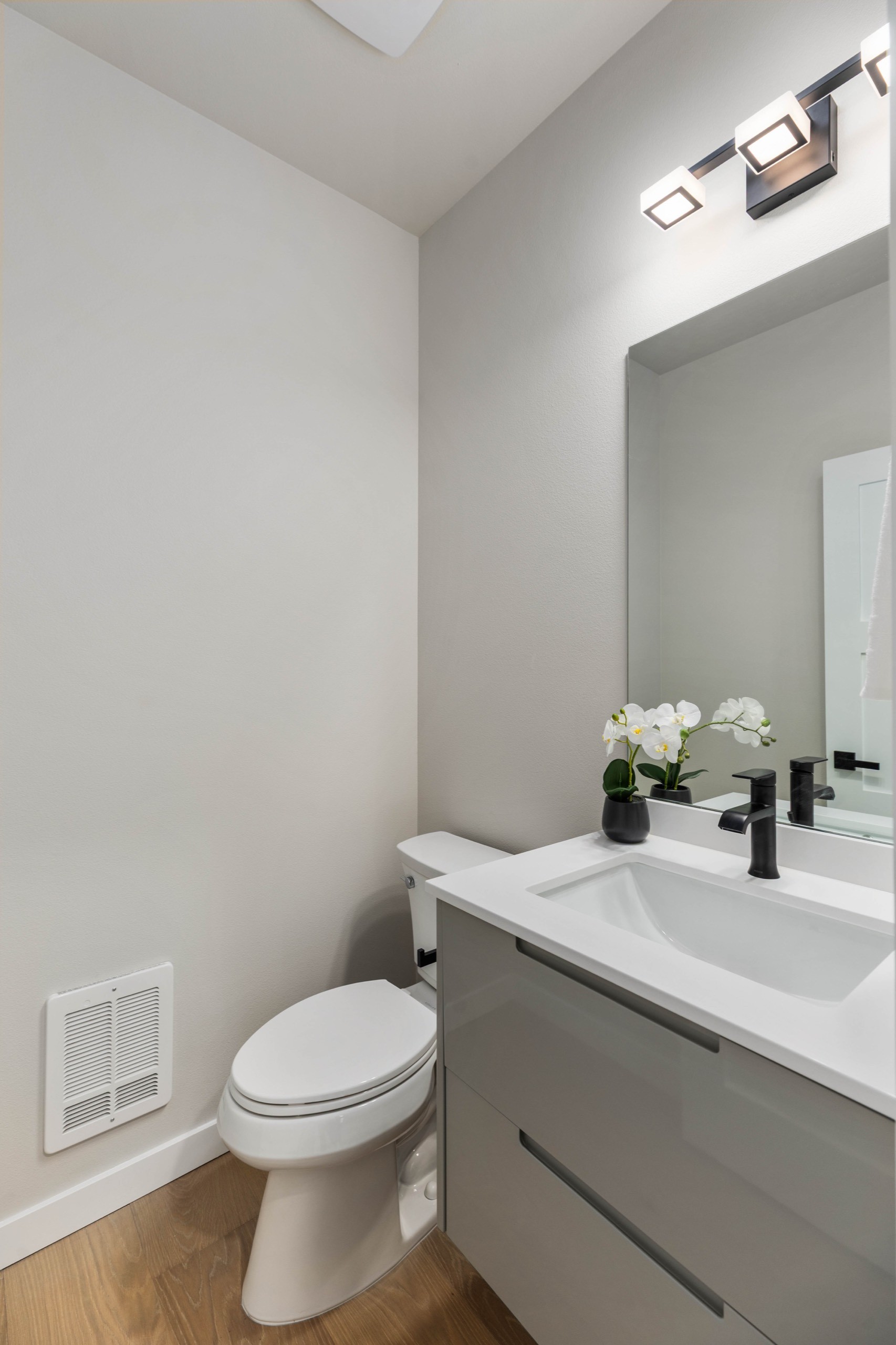 Minimalist luxury powder room with grey floating vanity, white quartz countertop, black matte faucet, large mirror, and soft recessed lighting