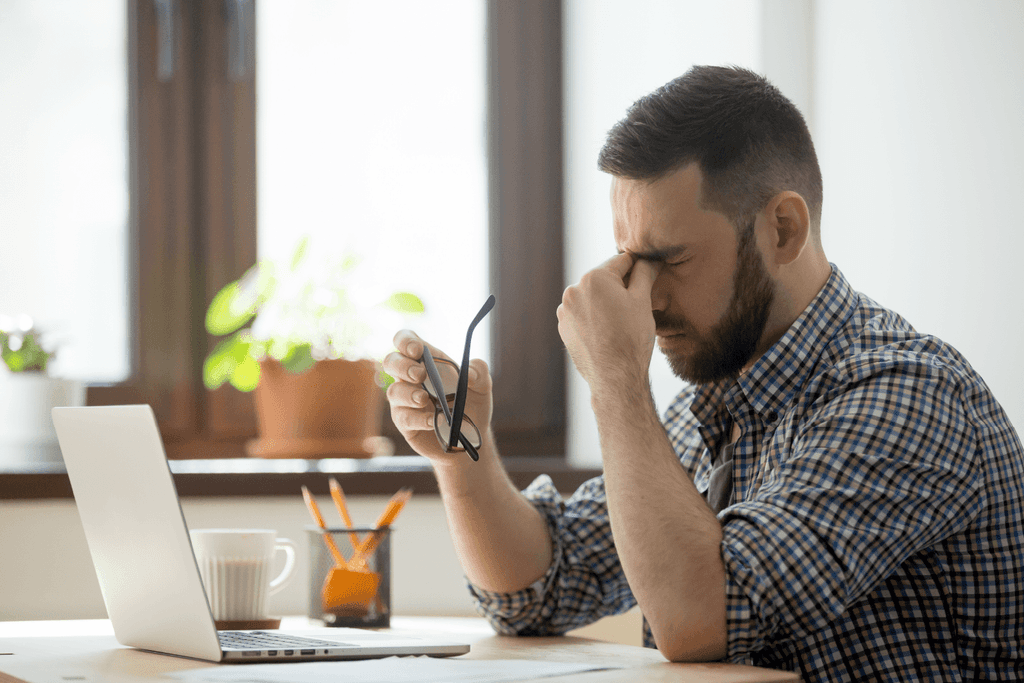 Homem com expressão cansada diante do computador, representando dificuldades com suporte de TI - FindUP soluções para problemas comuns de TI