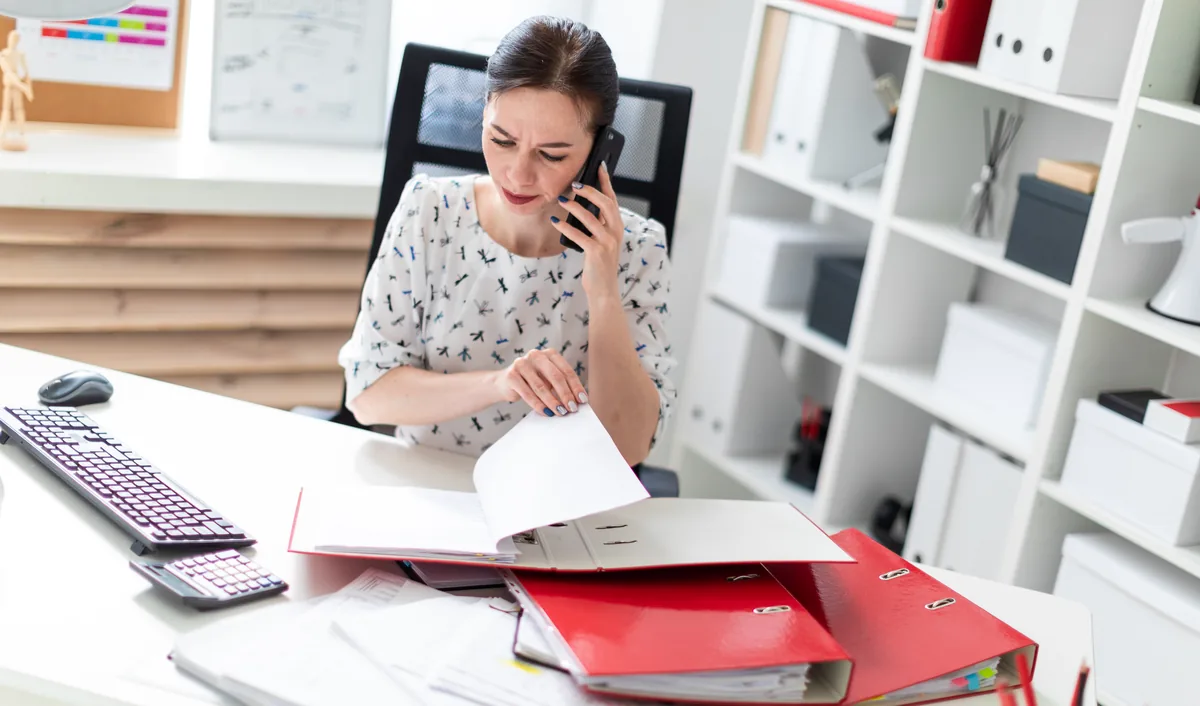 Office staff member on the phone while going through folders of paperwork