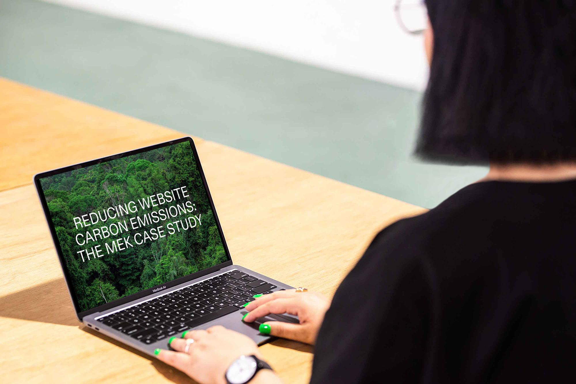 Environment and tech impact: A woman using a laptop displaying green code, representing a 67% reduction in website carbon emissions.