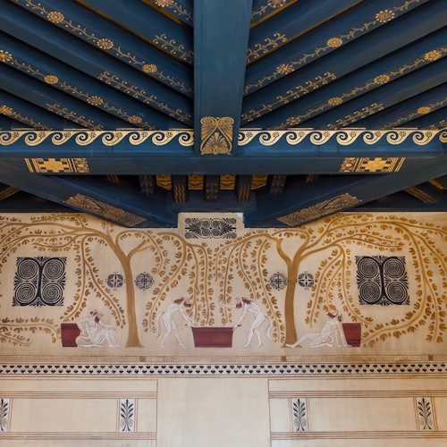 Ornate blue and gold decorated ceiling with a mural of people tending red planters, framed by intricate, stylized trees and patterns.