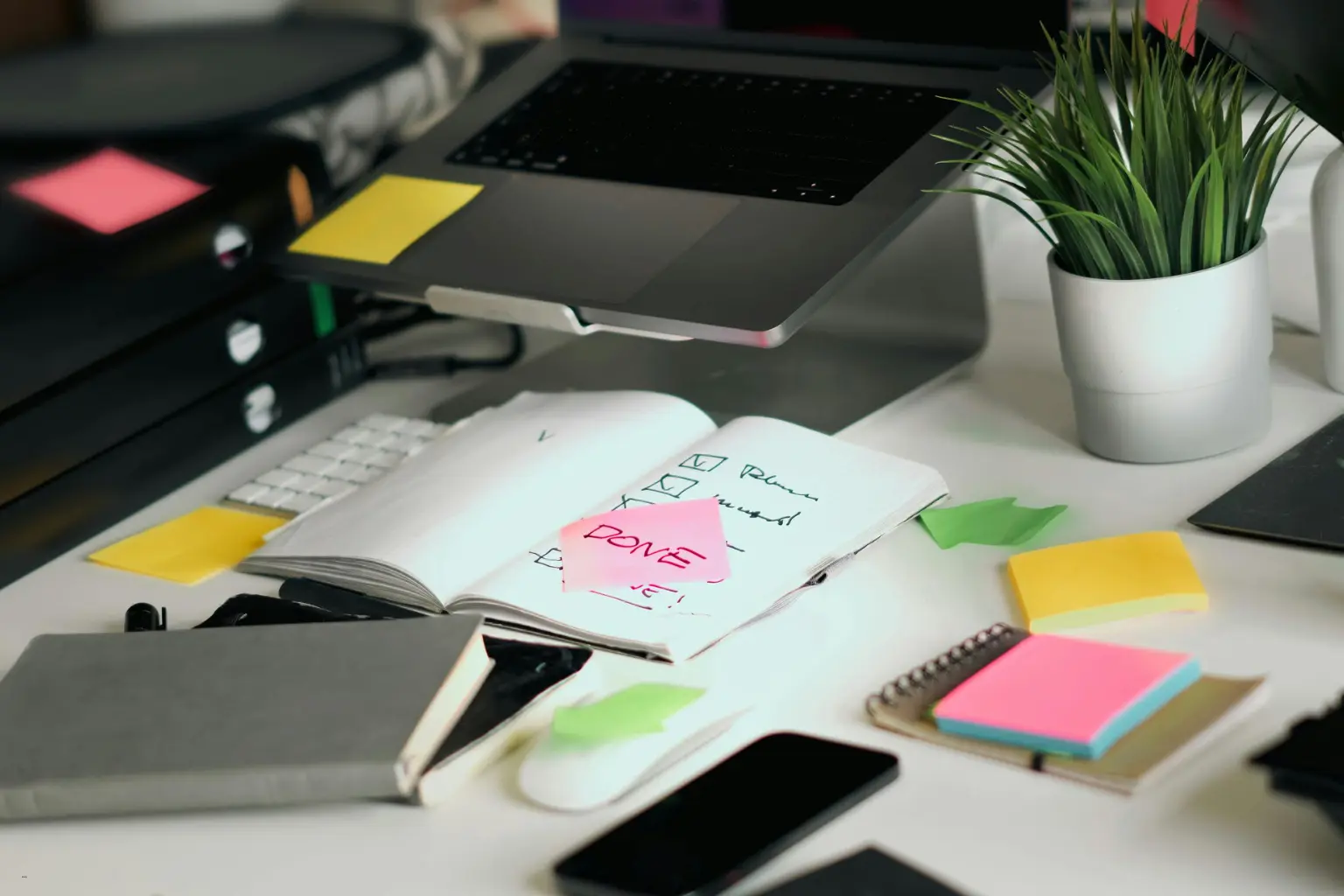 Automated scheduling software workspace with a laptop, notebooks, sticky notes, and a checklist marked “DONE.”