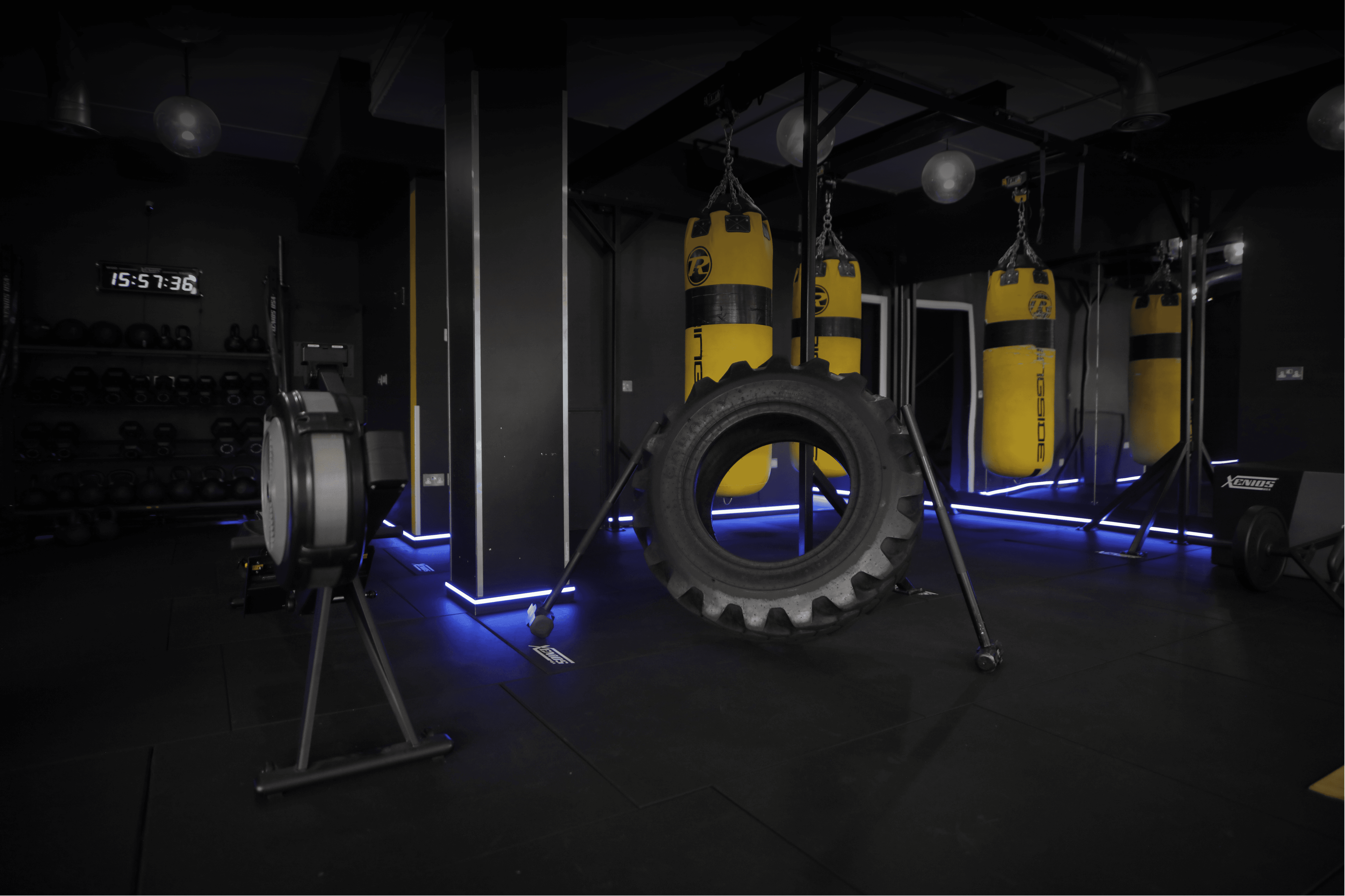 A dark, industrial-style gym space featuring a large black tractor tire and yellow heavy punching bags. Text reads: ARMORY with a Learn More button.
