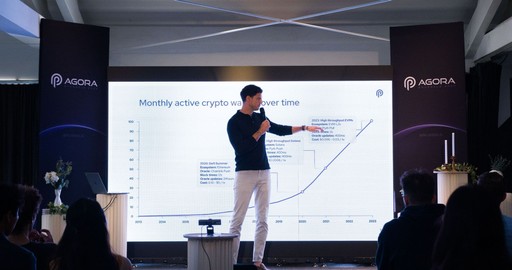 A speaker gestures towards a presentation on a large screen during a conference or seminar.