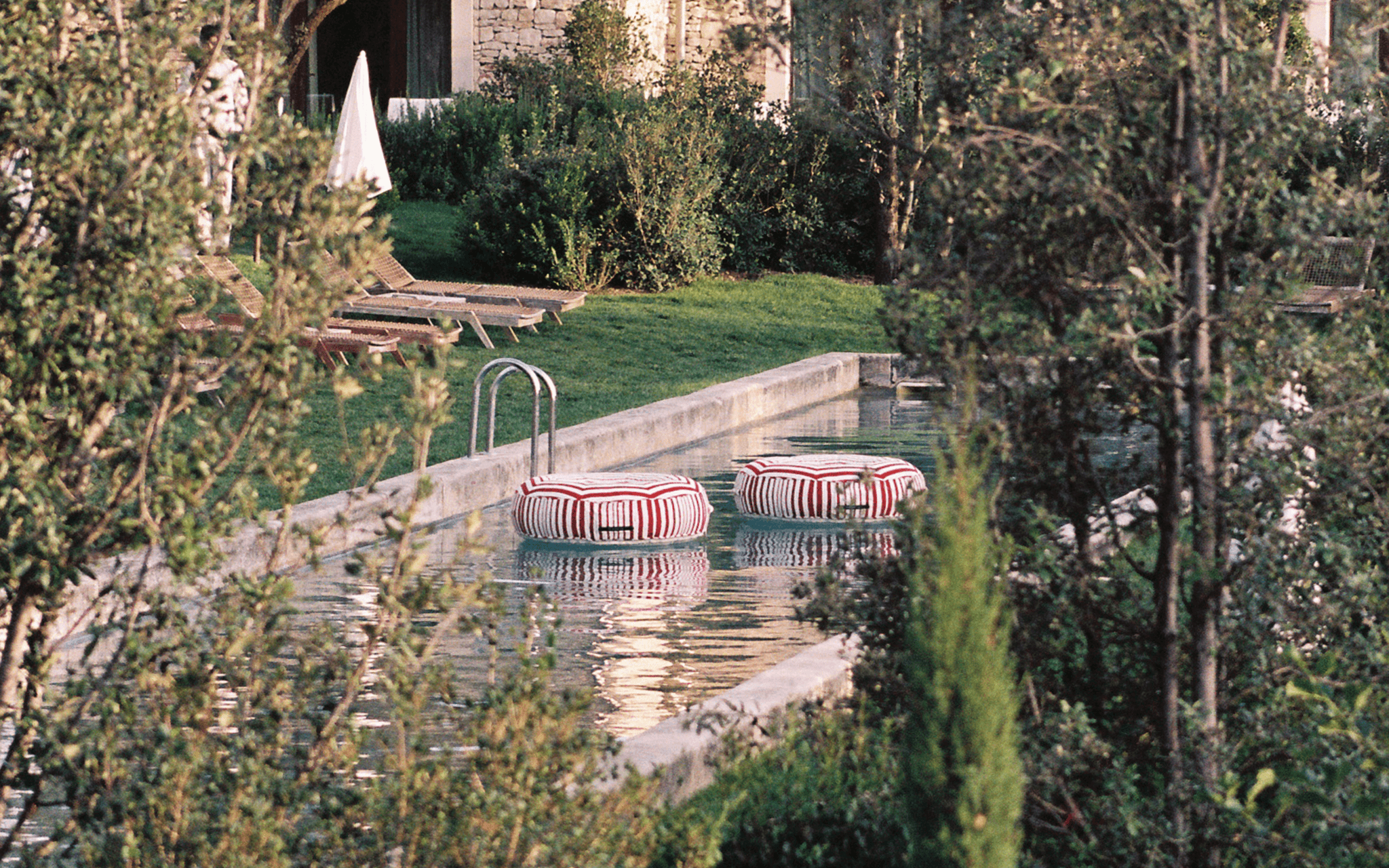 Two multi-colour striped ring pool floats floating in a stone-edged garden pool surrounded by greenery