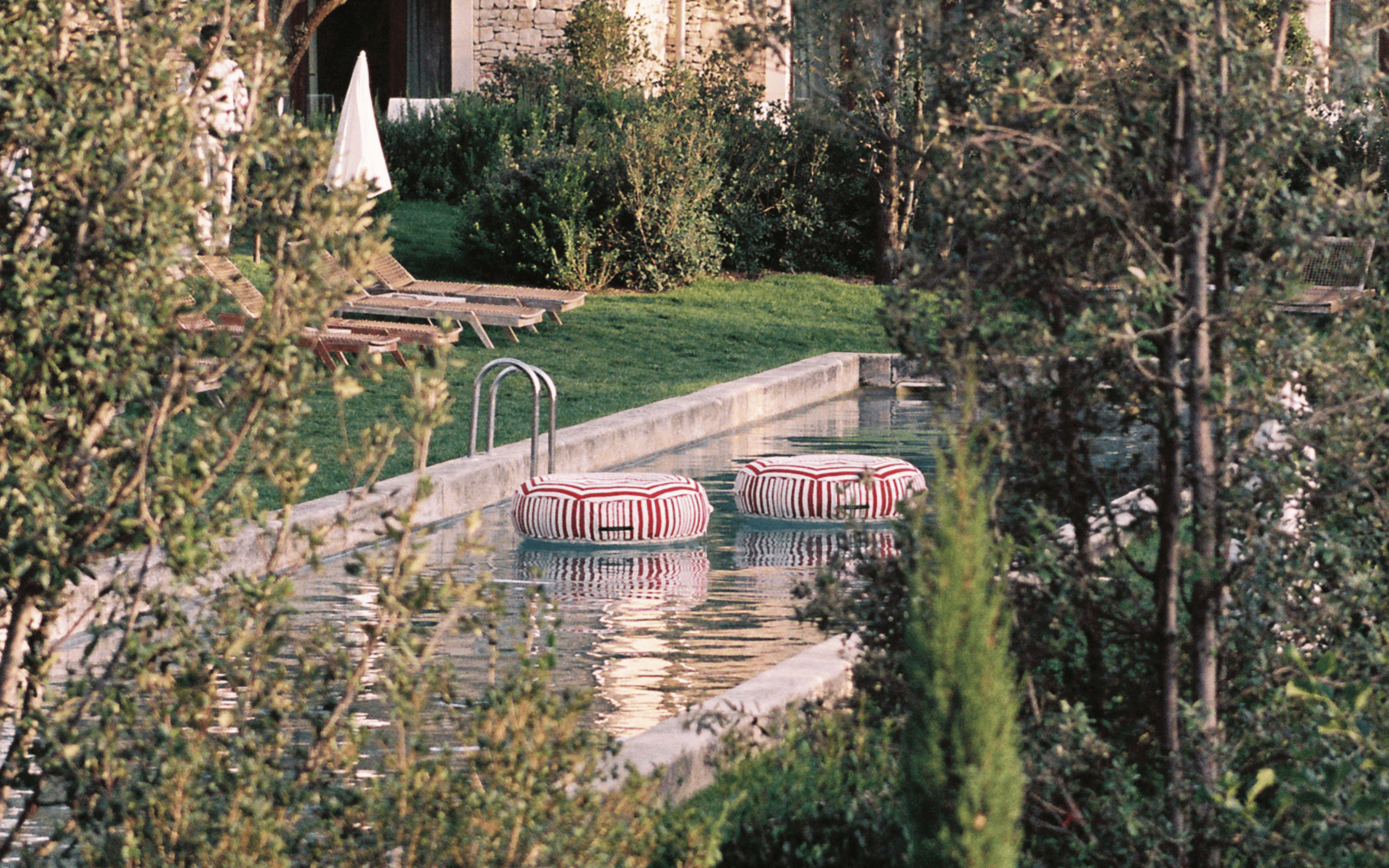 Two multi-colour striped ring pool floats floating in a stone-edged garden pool surrounded by greenery