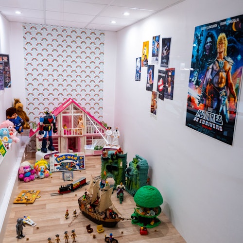 Ett lekrum för barn med leksaker, ett dockskåp, actionfigurer och affischer på väggarna. Golvet är belamrat med olika lekset.