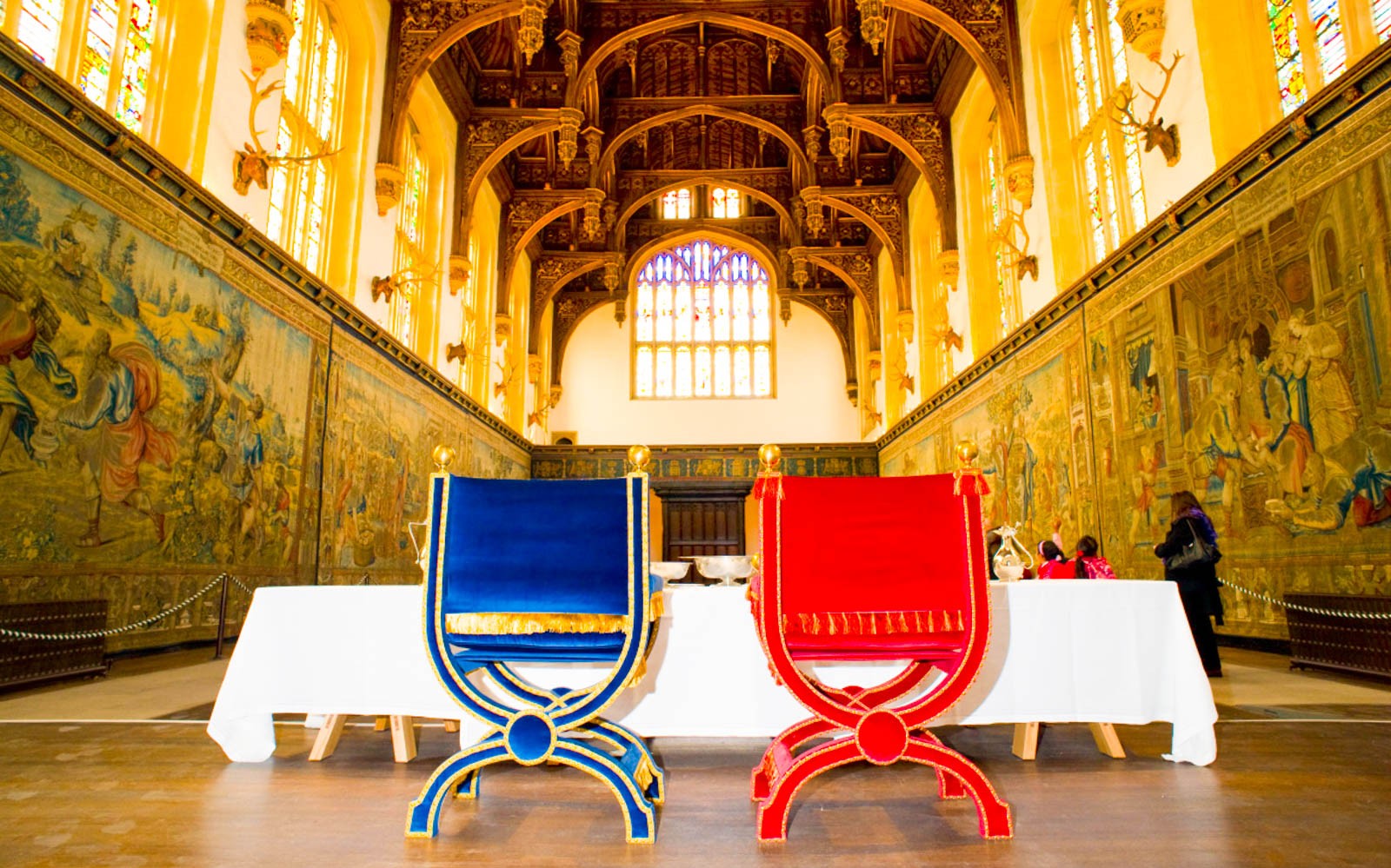 ਹੈਂਪਟਨ ਕੋਰਟ ਪੈਲੇਸ, ਲੰਡਨ ਦੇ ਮਹਾਨ ਹਾਲ ਦੇ ਅੰਦਰ ਗੱਲਬਾਤ ਕਰ ਰਹੇ ਦ੍ਰਸ਼ਕ, ਇਤਿਹਾਸਕ ਟੈਪਸਟਰੀਆਂ ਦੇਖ ਰਹੇ ਹਨ।