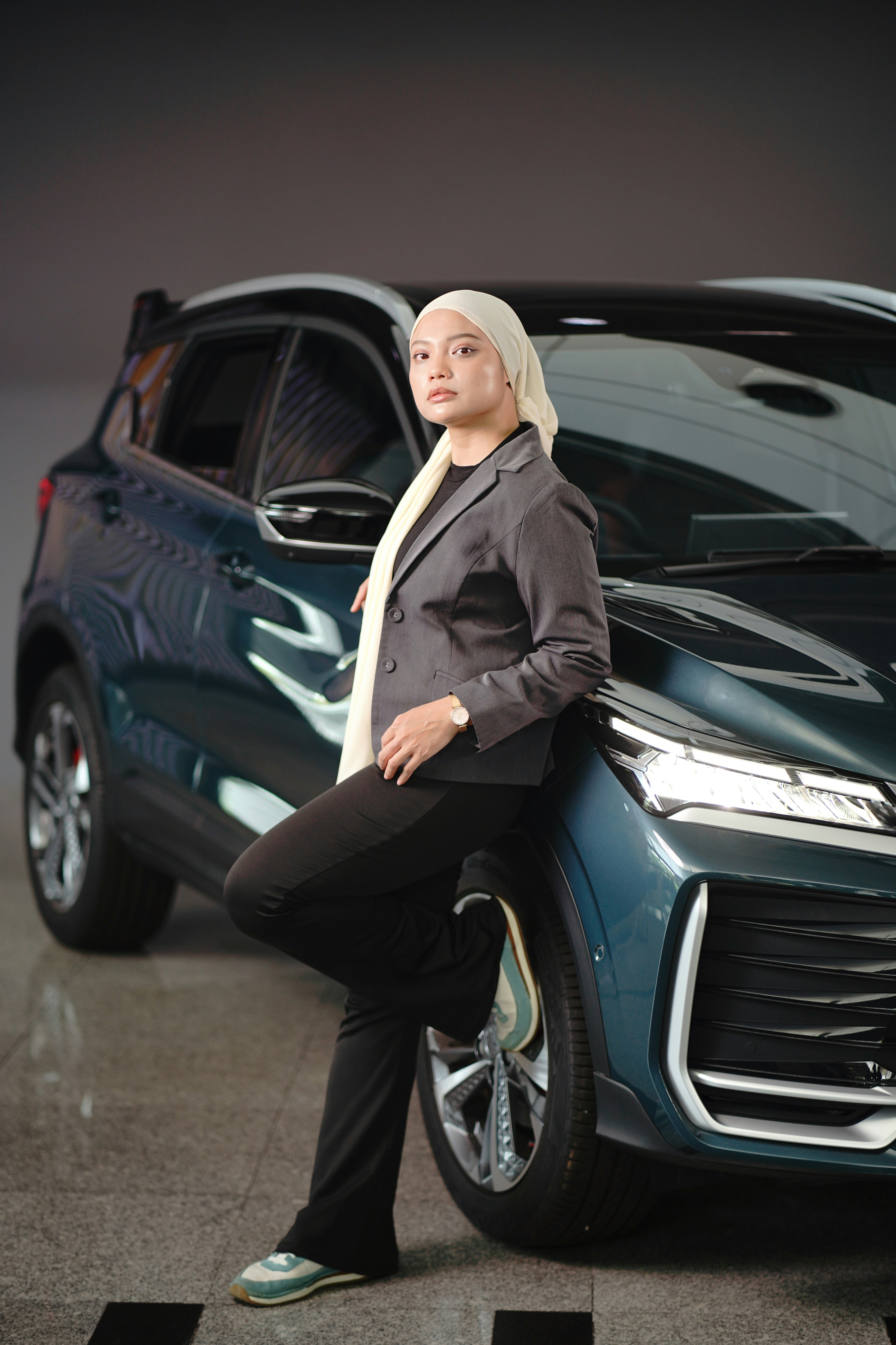 Woman in a blazer poses by a new car.