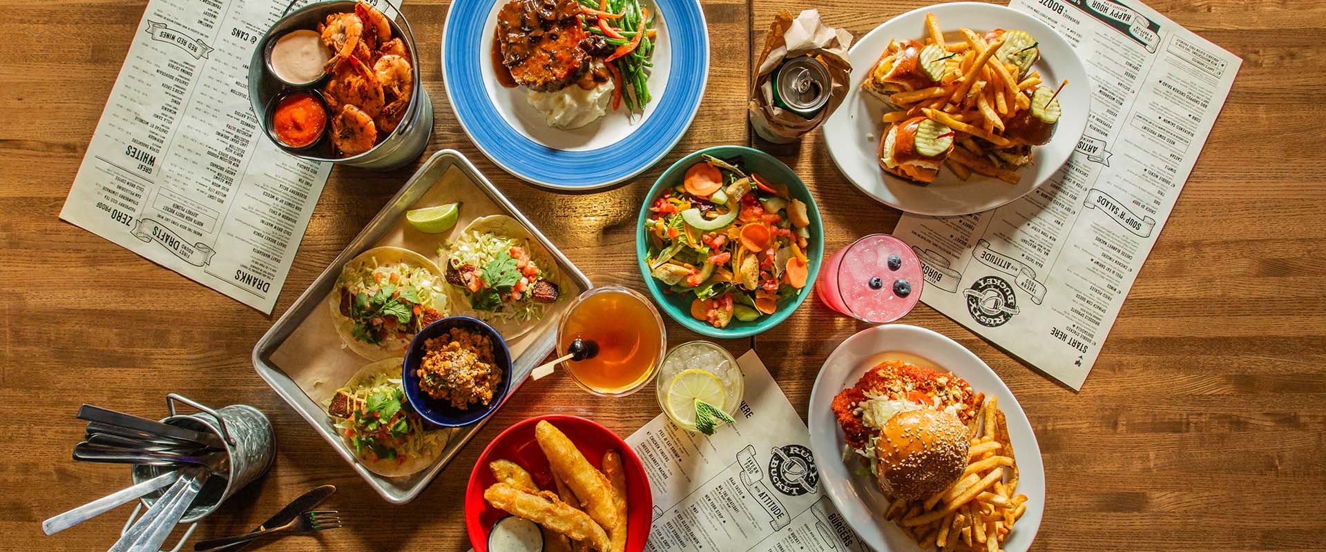 Overhead view of tacos, wings, burgers, fries and drinks on a wood table at Rusty Bucket Clintonville