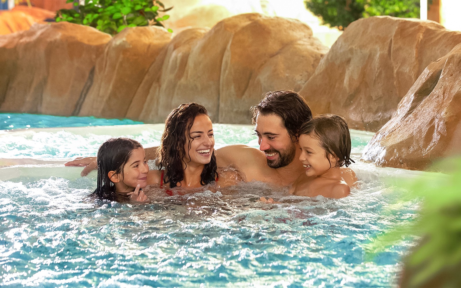Family relaxing in a pool at Aqualibi, surrounded by rocks and greenery.