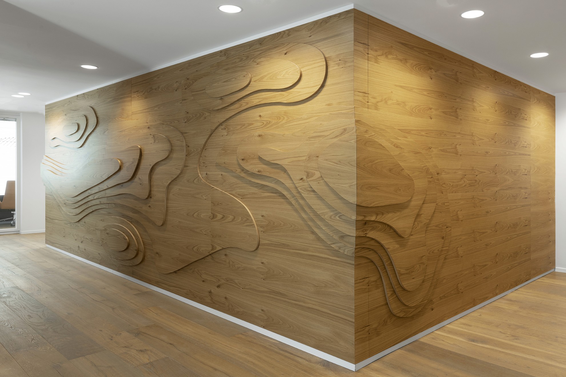 נגרות אדריכלית: קיר כוח פינתי בחיפוי עץ CNC, הממחיש את קווי הגובה הטופוגרפיים (Contour Lines) והופך את הנתונים הגיאולוגיים לאלמנט עיצובי.