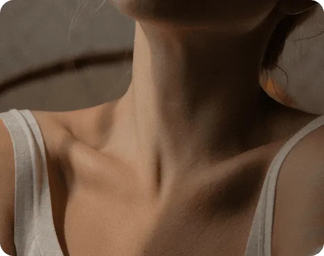 A close-up of a person's neck and shoulder, partially shown, with soft lighting and a neutral background.