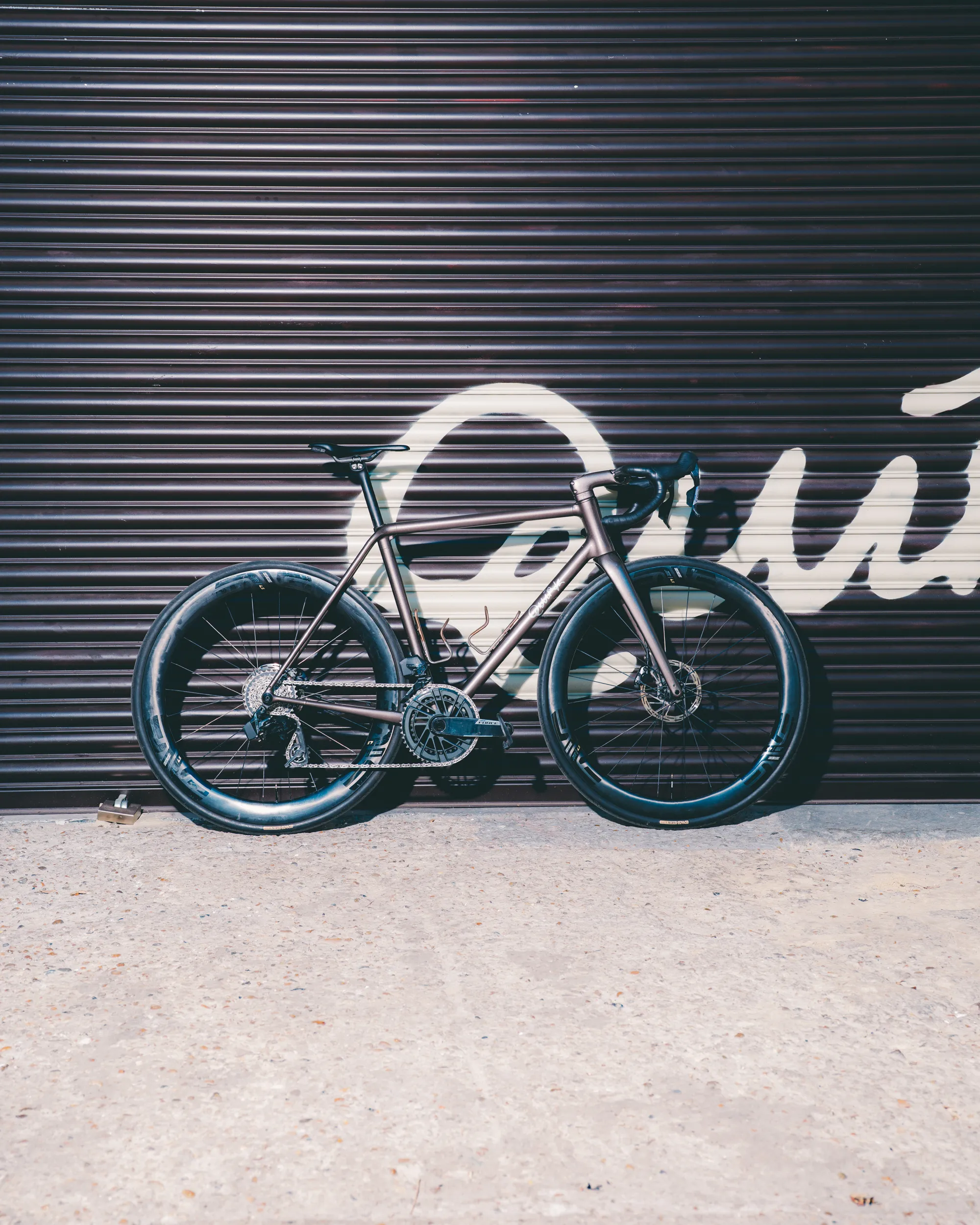 Light blue Quirk Cycles Durmitor road bike in a workshop with dark wheels