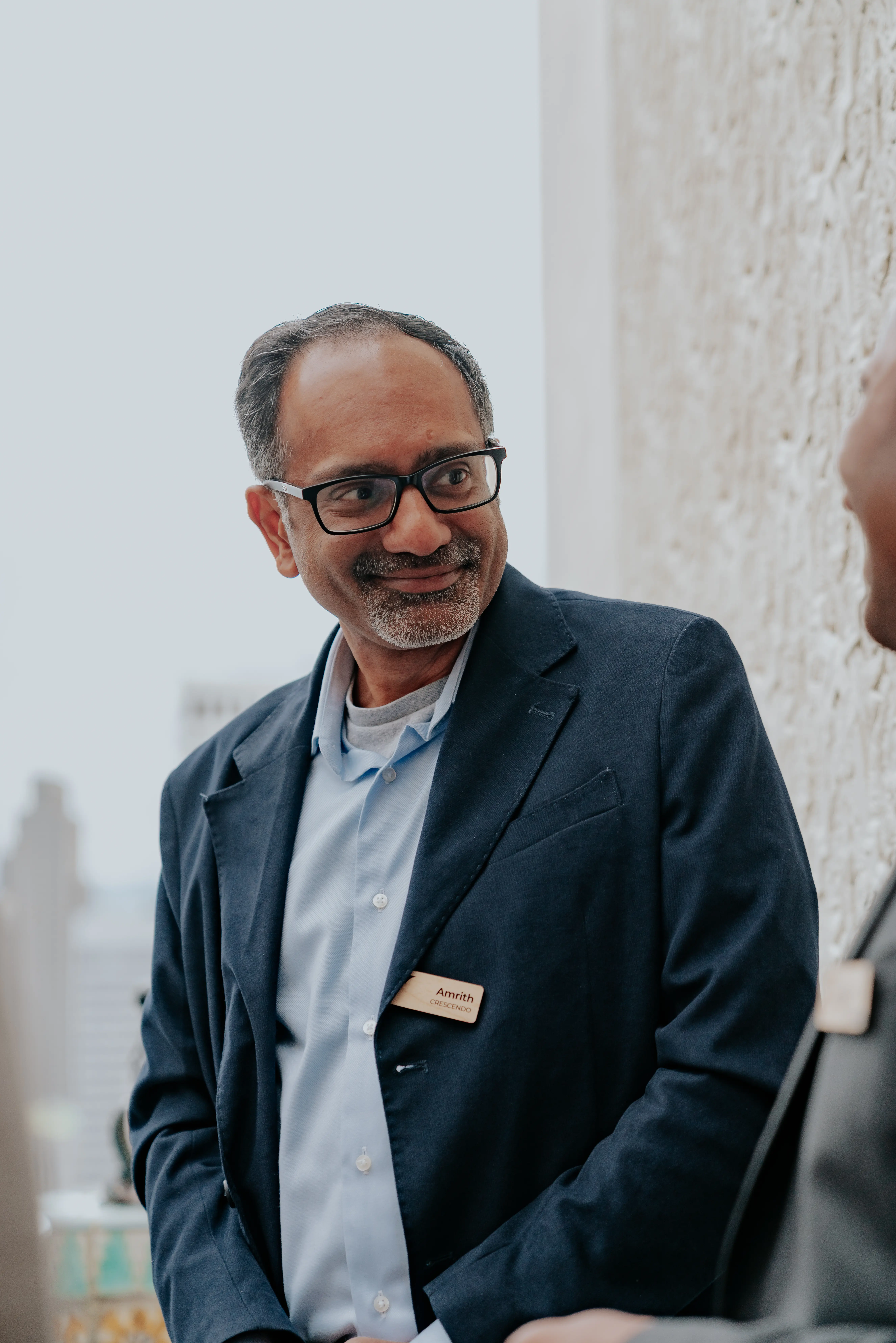 Person wearing glasses and a suit sitting at an outdoor table.
