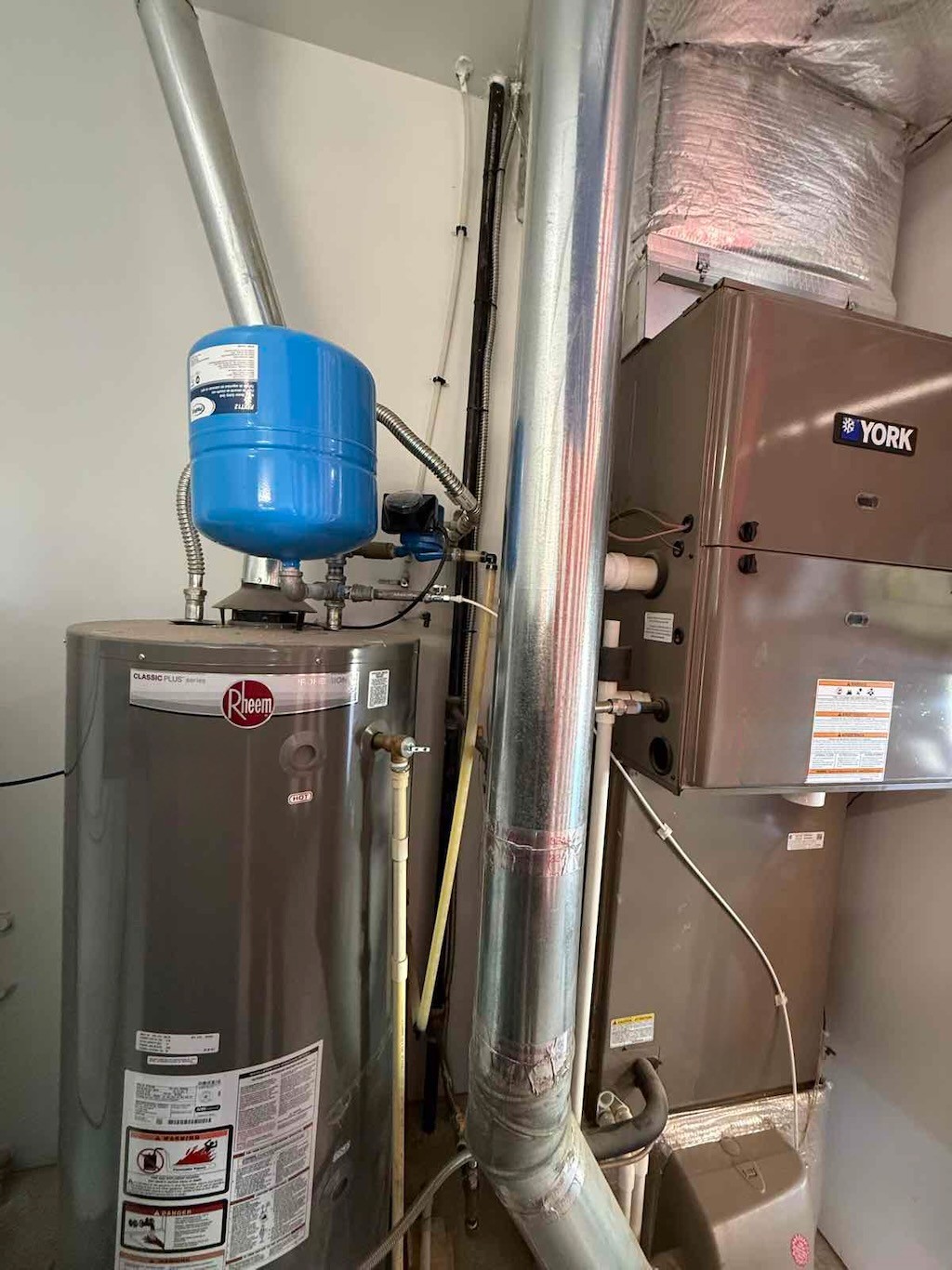Gas water heater with expansion tank and recirculating pump beside a furnace in a Garden City garage mechanical corner.