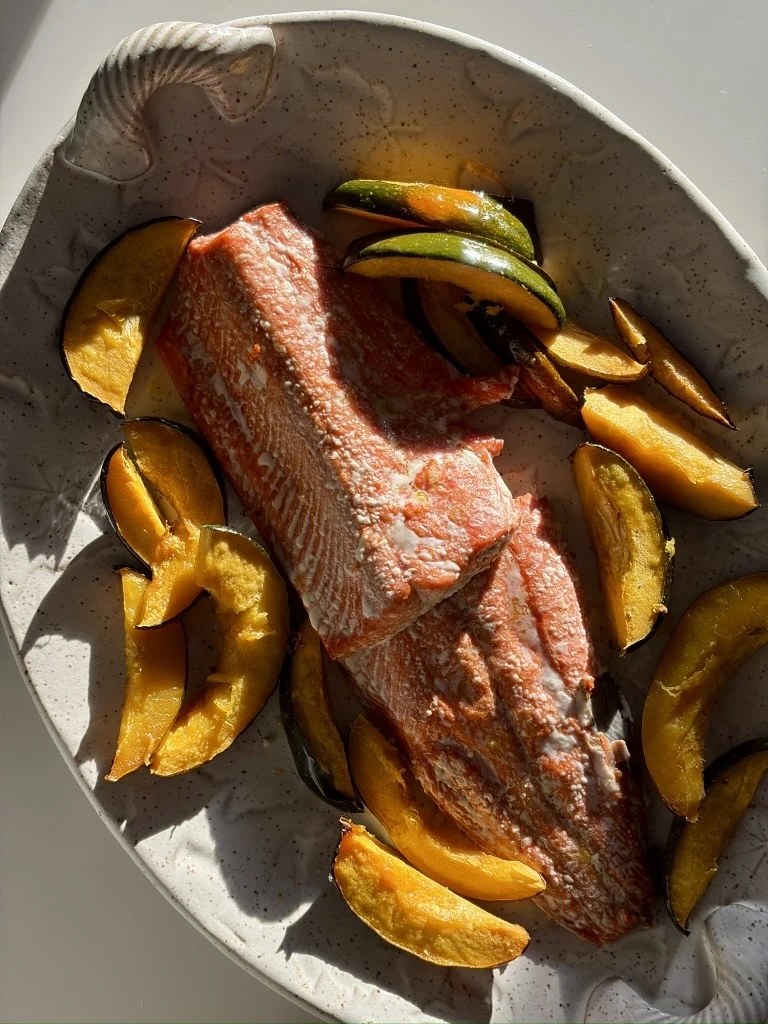 A plated serving of roasted maple-glazed acorn squash alongside a cooked salmon fillet, both golden and caramelized, arranged neatly on a white plate with a simple, clean presentation.