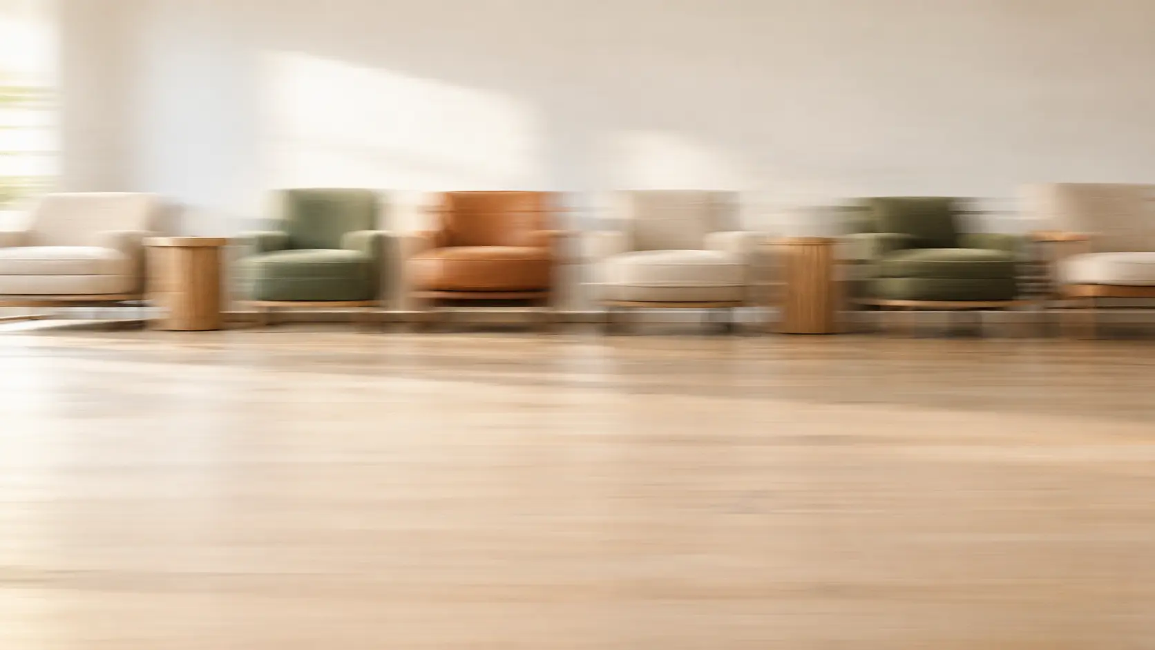 Row of lounge chairs and oak side tables in a bright room, softly blurred by motion