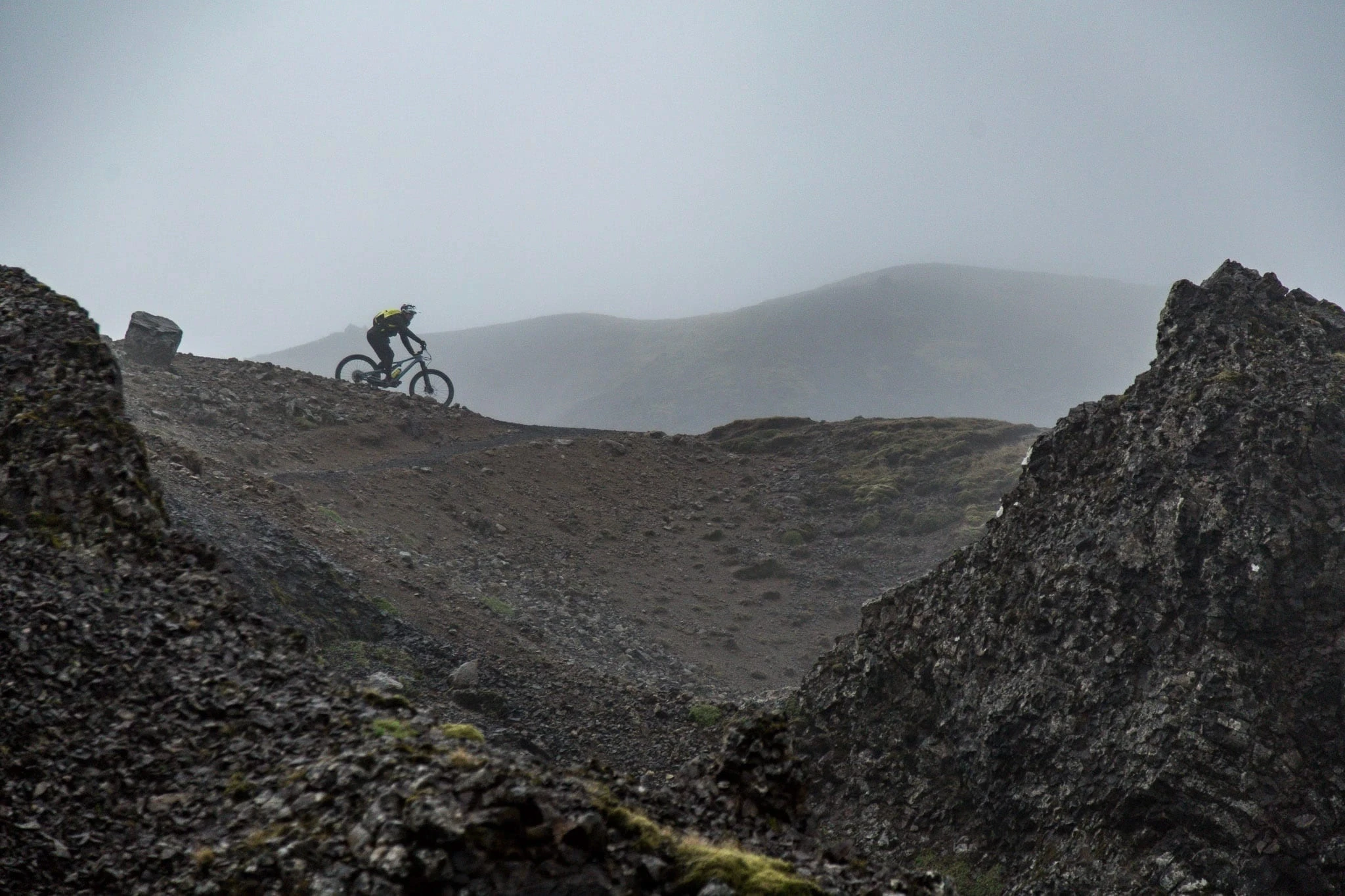 Mountain biker riding along a ridgeline in misty volcanic terrain.