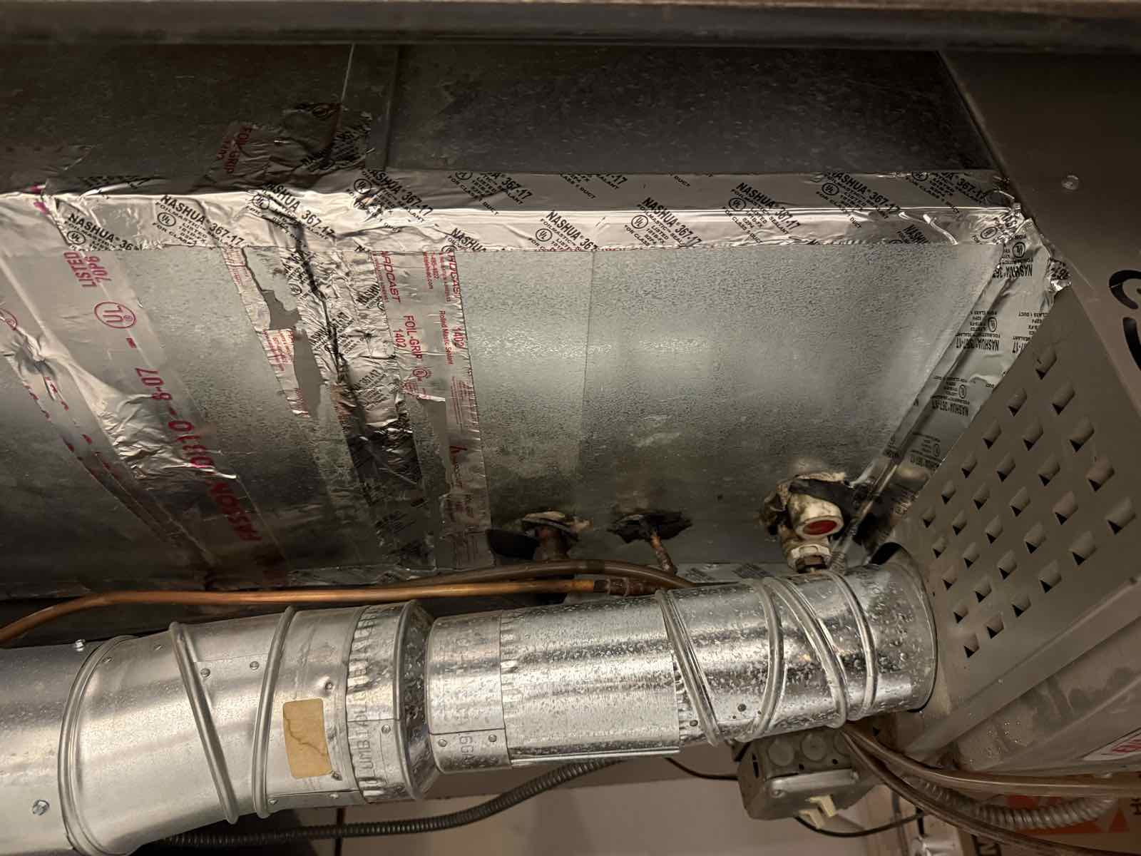 The side of a furnace cabinet and plenum, with an old condensate drain fitting exiting through the sheet metal near the base.